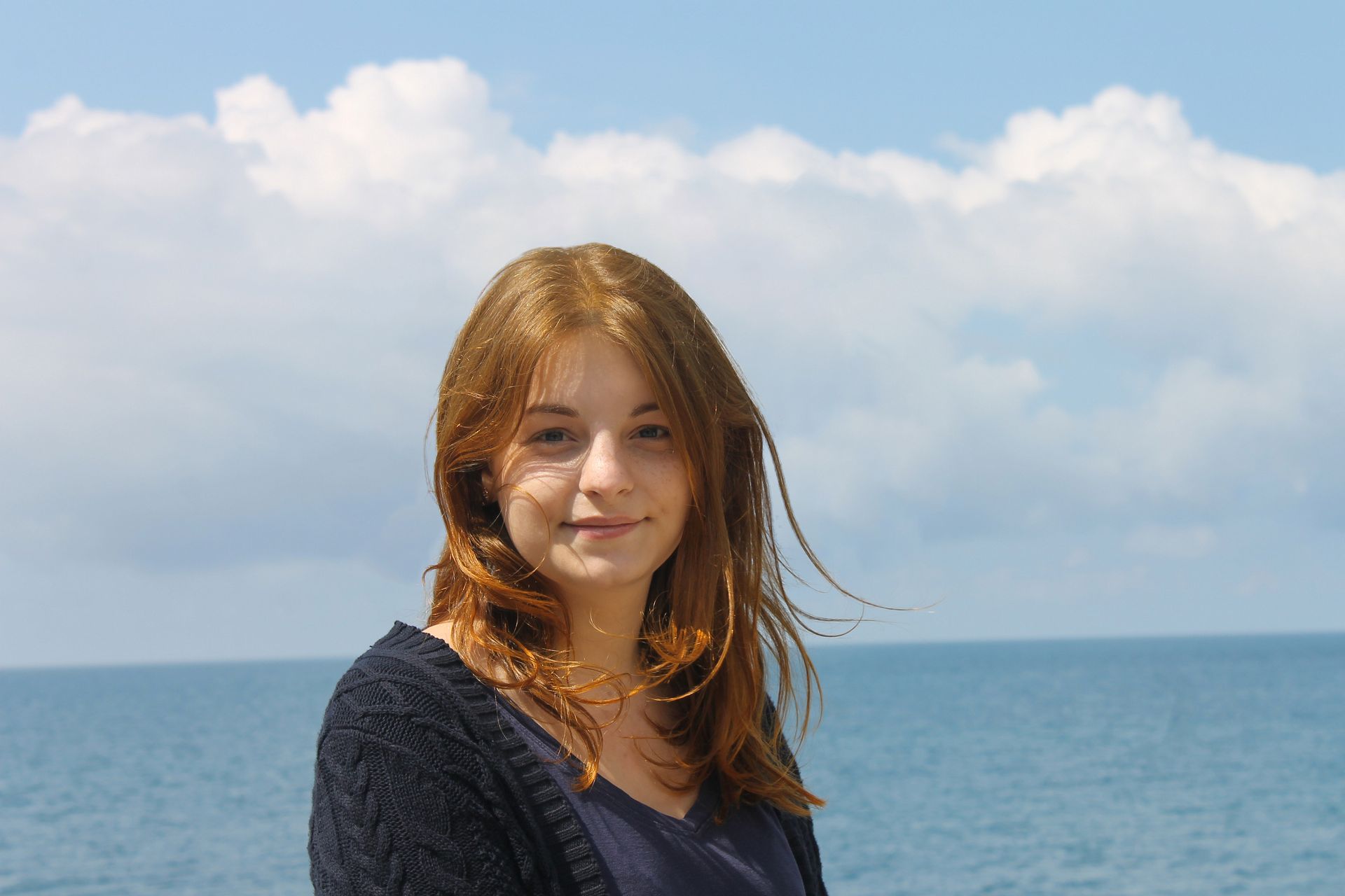 A young woman is standing in front of the ocean.