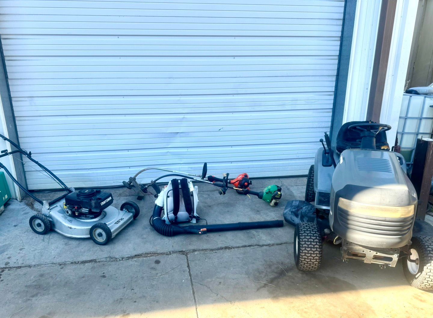 Man mowing a green lawn in a sunny garden, wearing work clothes and a green hat.