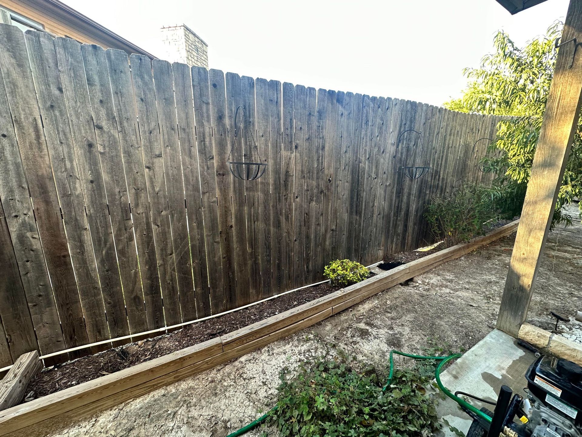 A wooden fence in a backyard with a hose in front of it.