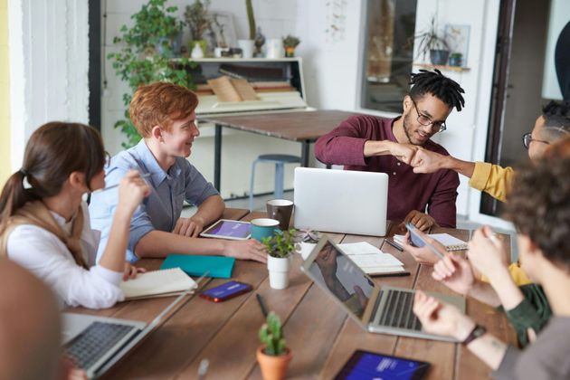 A group of people are sitting around a table with laptops.