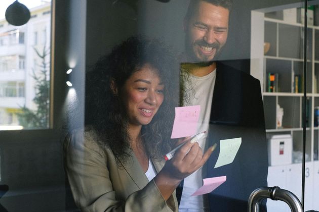 A man and a woman are looking at sticky notes on a glass wall.