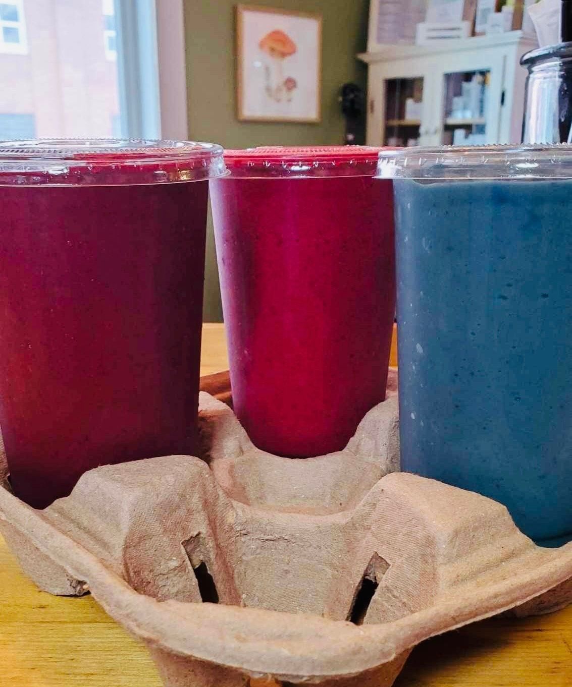 Three cups of different colored drinks are in a cardboard tray on a table.