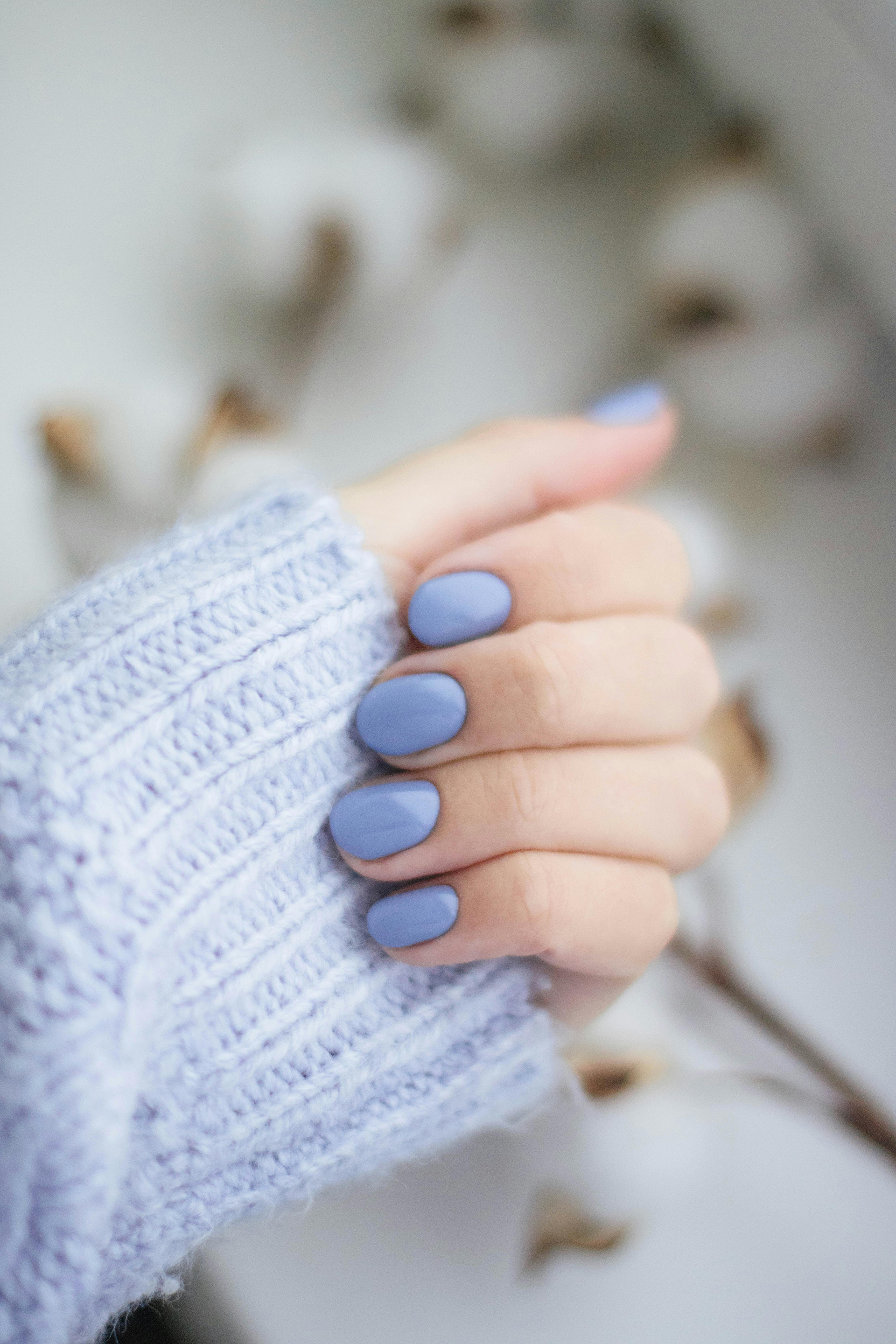 A close up of a woman 's hand with blue nails wearing a blue sweater.