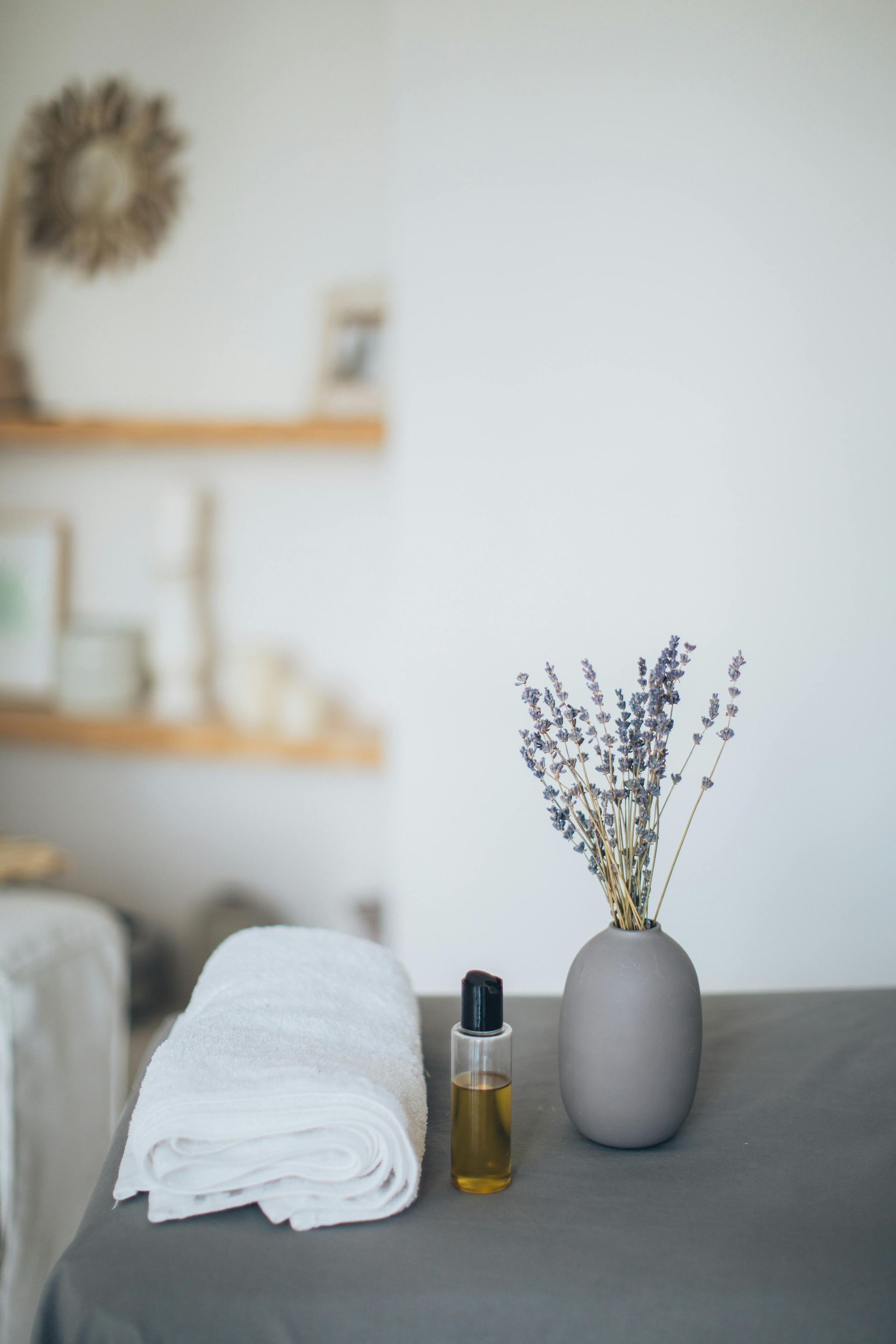 Massage table setup with rolled towel, essential oil, and lavender in a vase.
