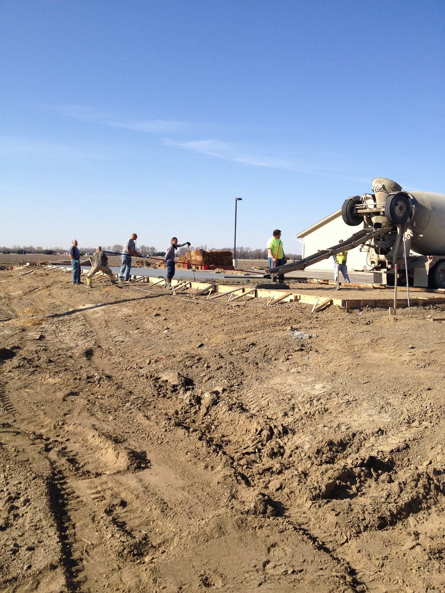 A concrete truck is pouring concrete into a dirt field.