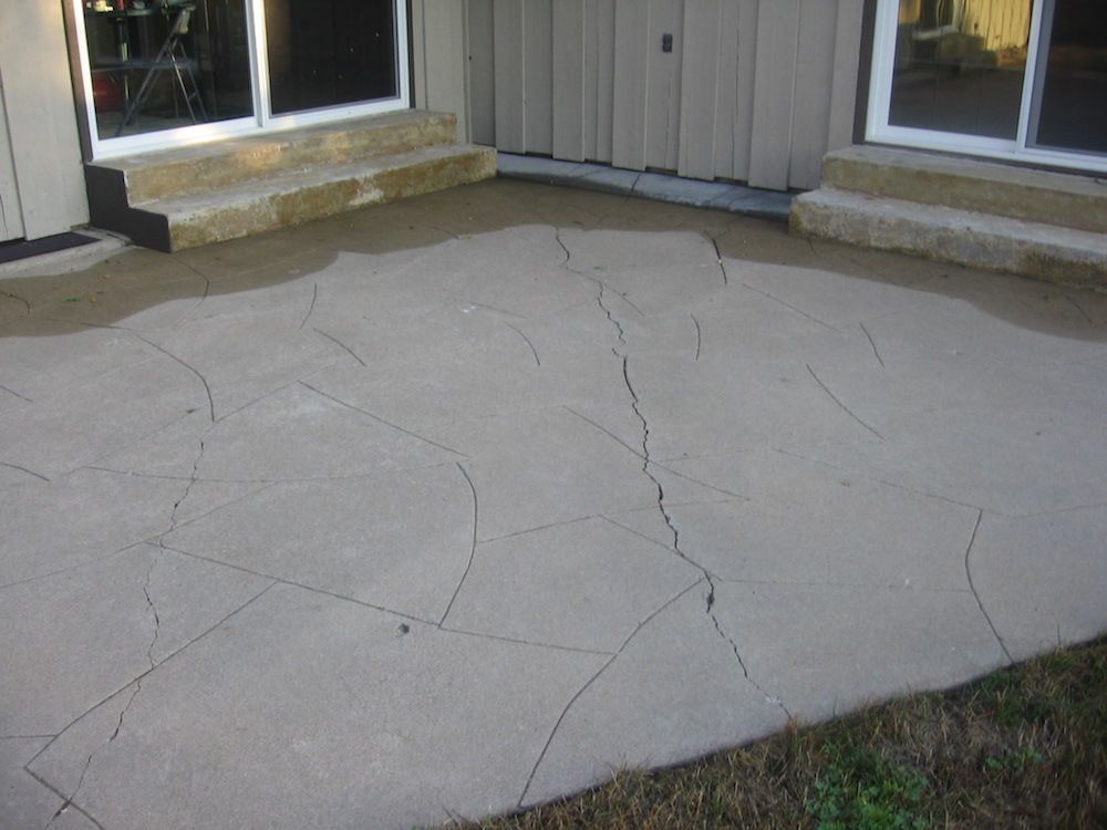 A cracked concrete patio in front of a house