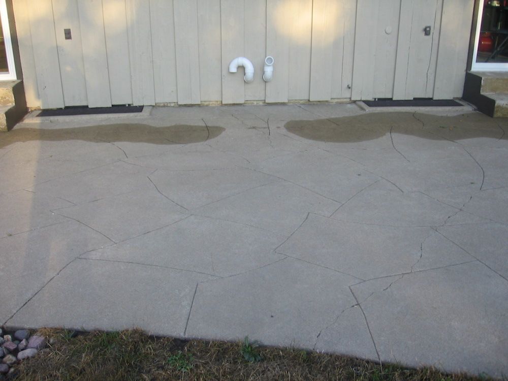 A concrete driveway in front of a garage with a pipe coming out of it.