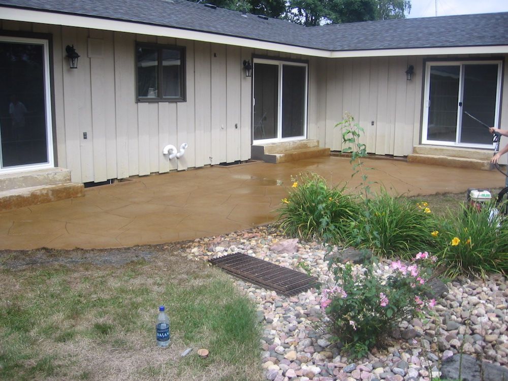 A person is spraying water on a patio in front of a house.