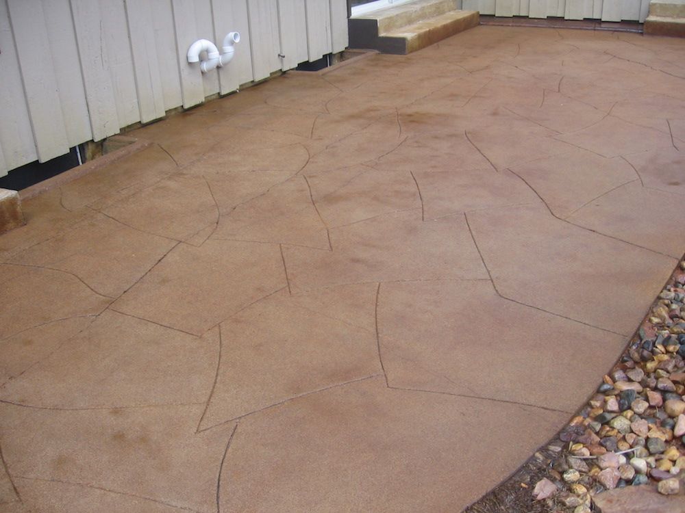 A brown concrete patio with a white fence in the background