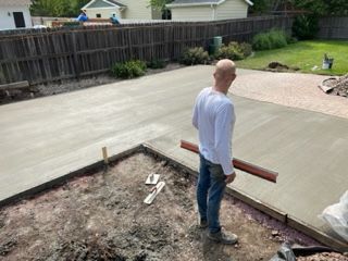 A man is standing on a concrete driveway holding a level.