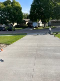 A man is painting a concrete driveway in a residential neighborhood.