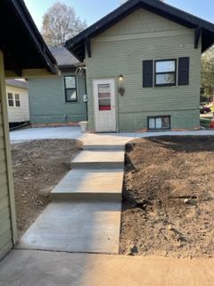 A concrete walkway leading to a house with a white door.