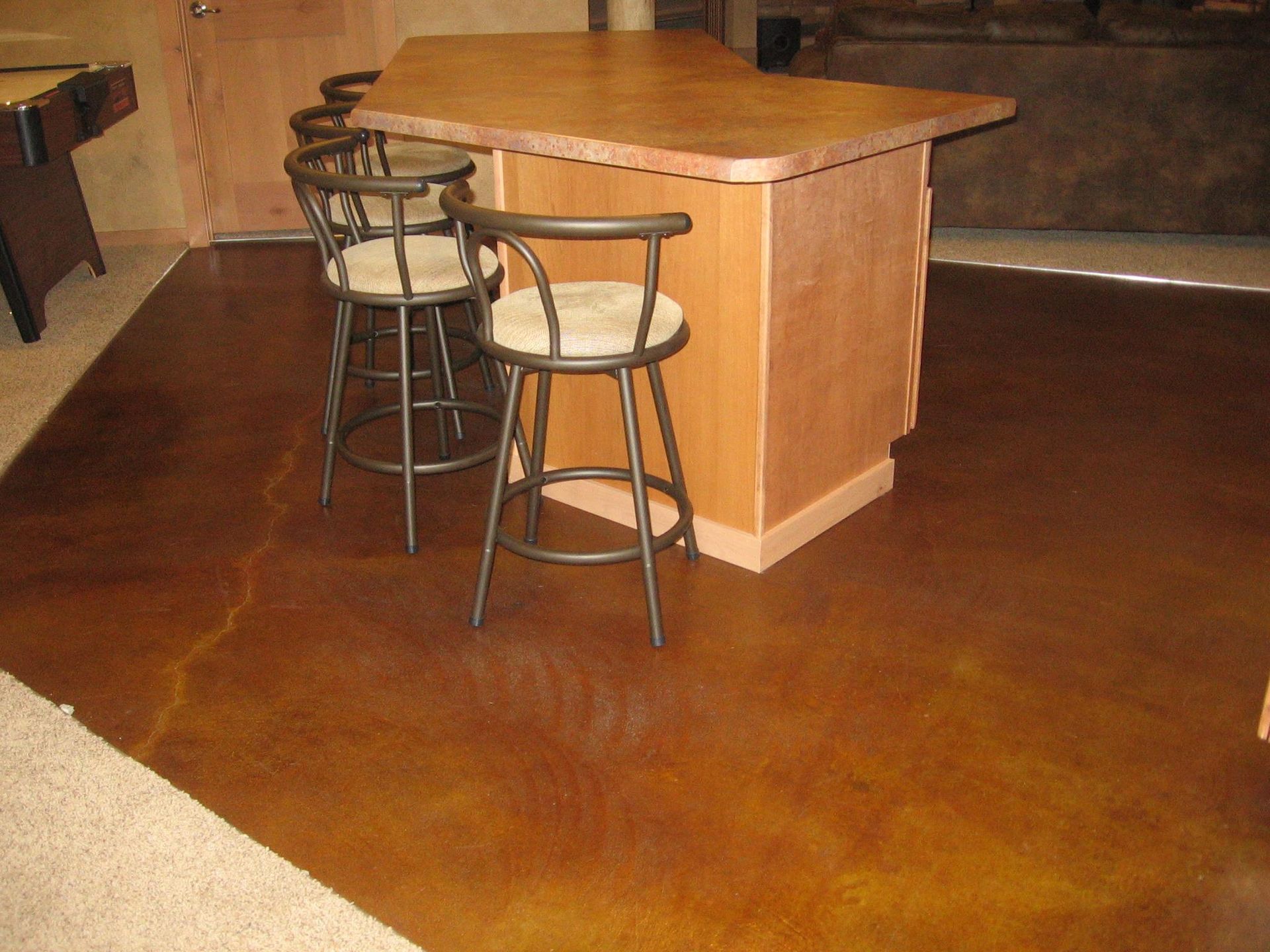 A bar with stools and a pool table in the background
