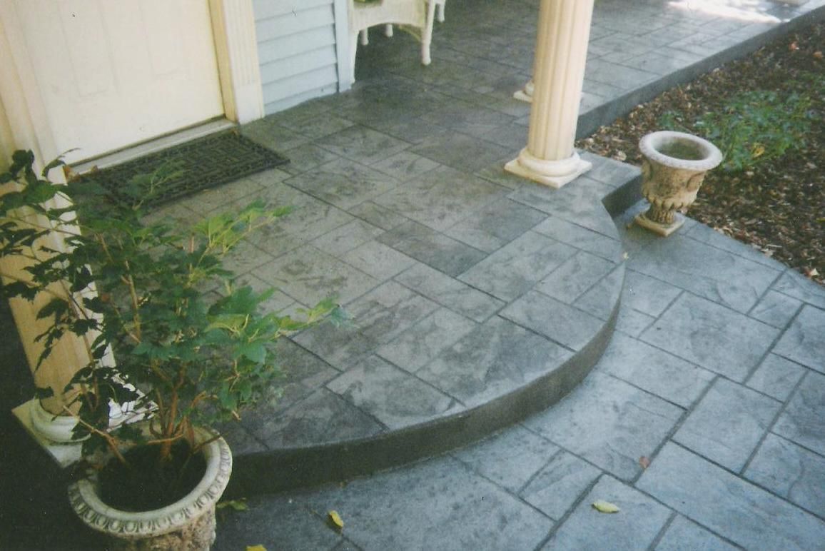 A concrete walkway leading to a porch with potted plants.