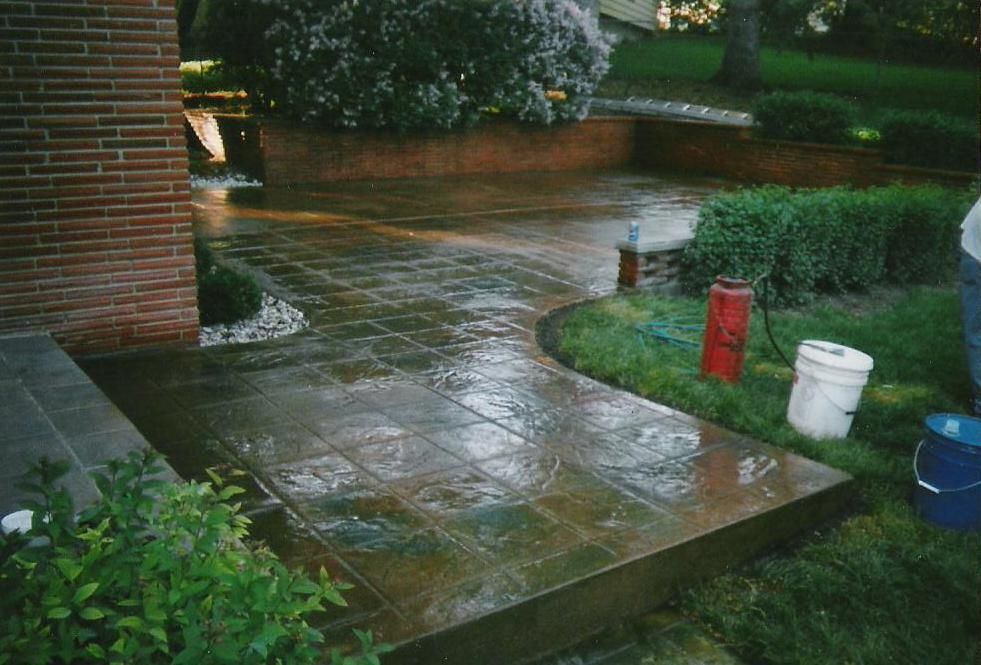 A person is standing on a concrete walkway next to a red bucket.