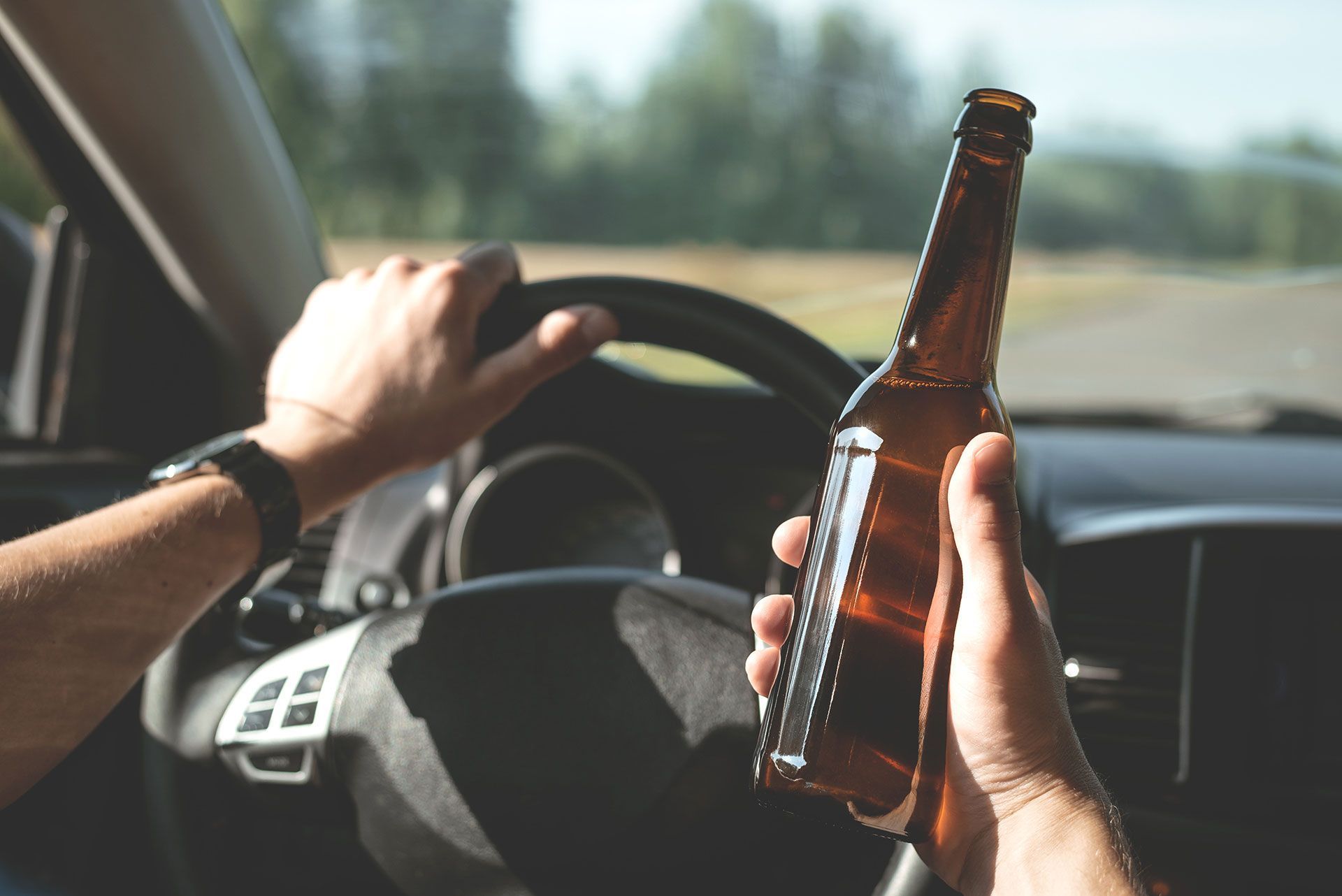 Driver is driving a car with a bottle of beer in hand. Drunk driving concept