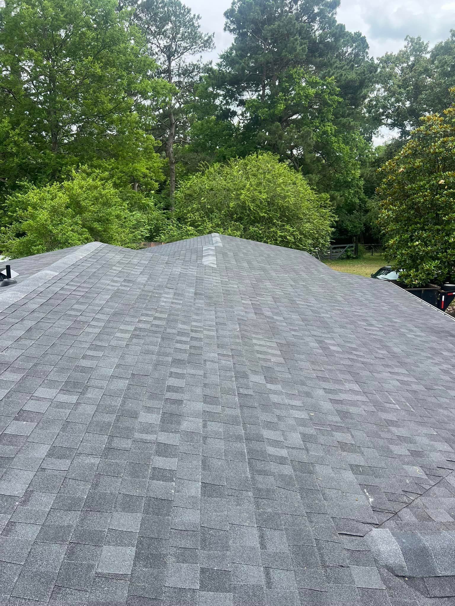 A roof with a chimney on it is surrounded by trees.