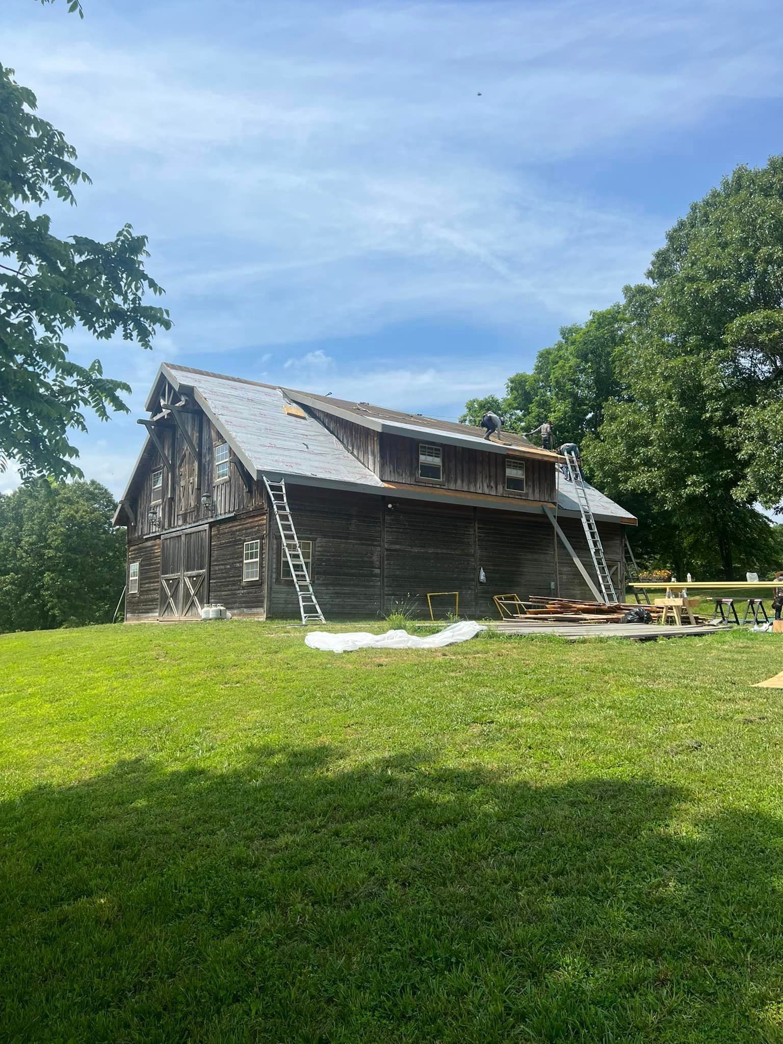 A large wooden barn is sitting on top of a grassy hill.