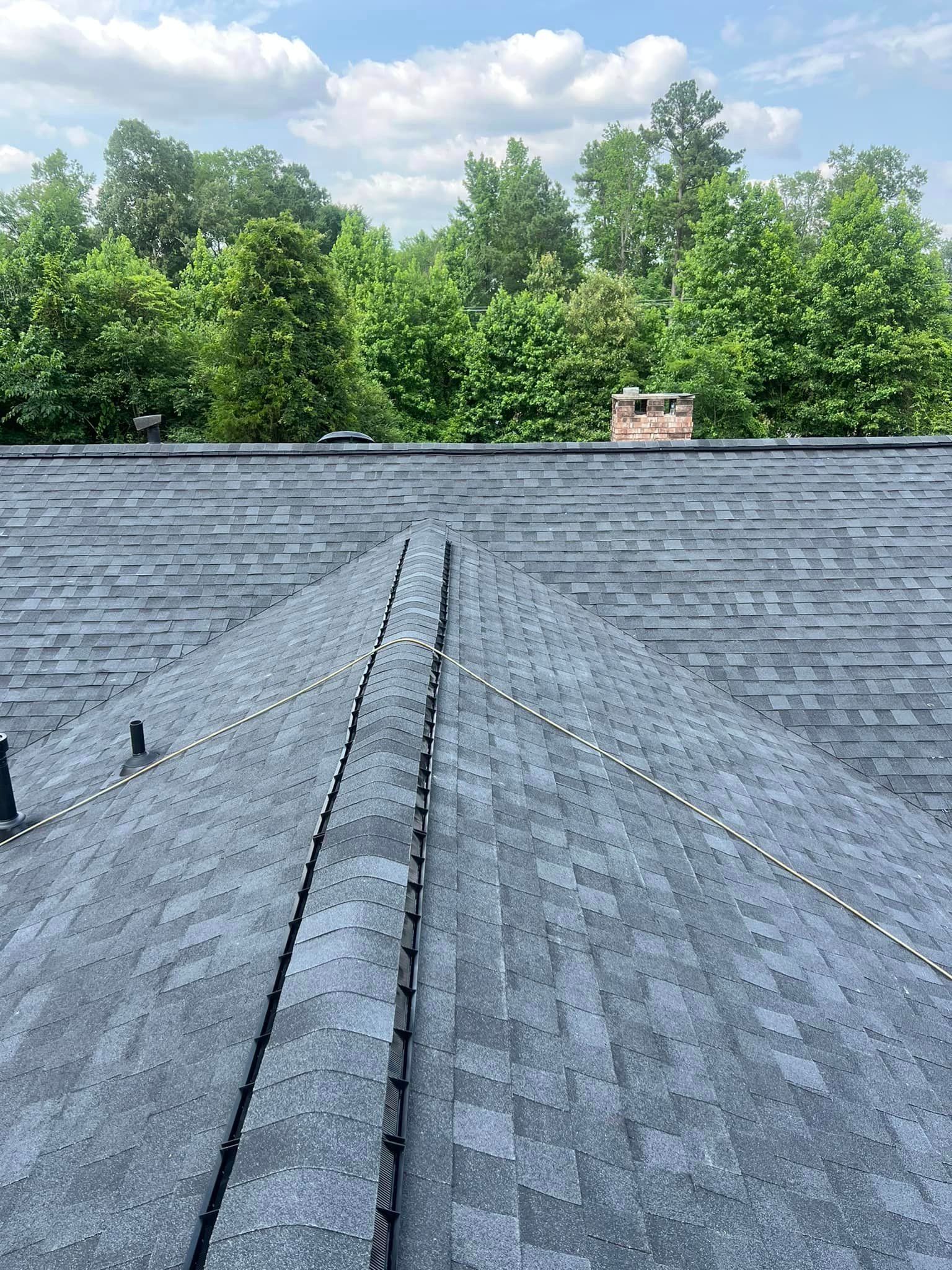 A close up of a roof with a chimney and trees in the background.