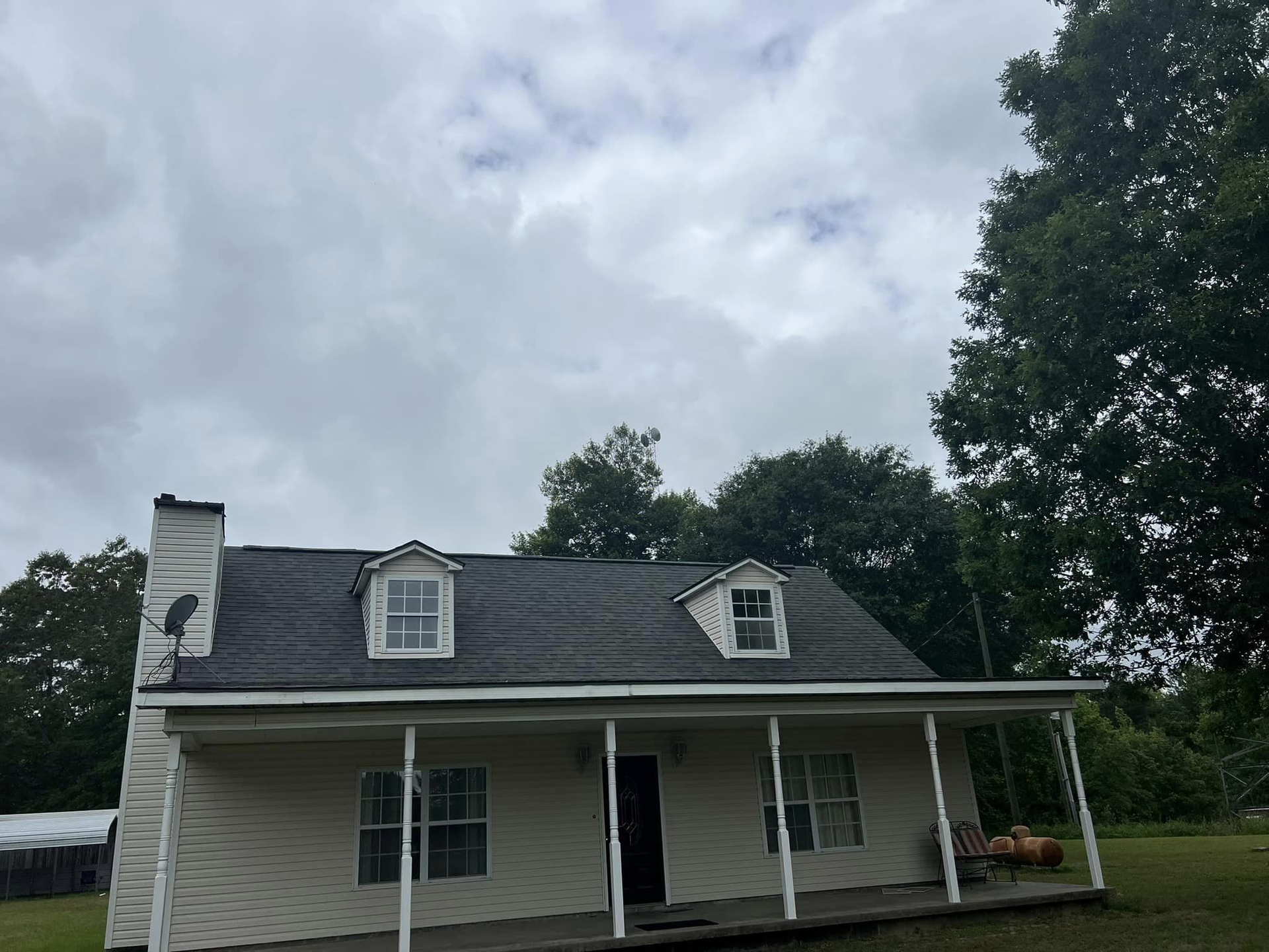 A white house with a black roof and a porch on a cloudy day.