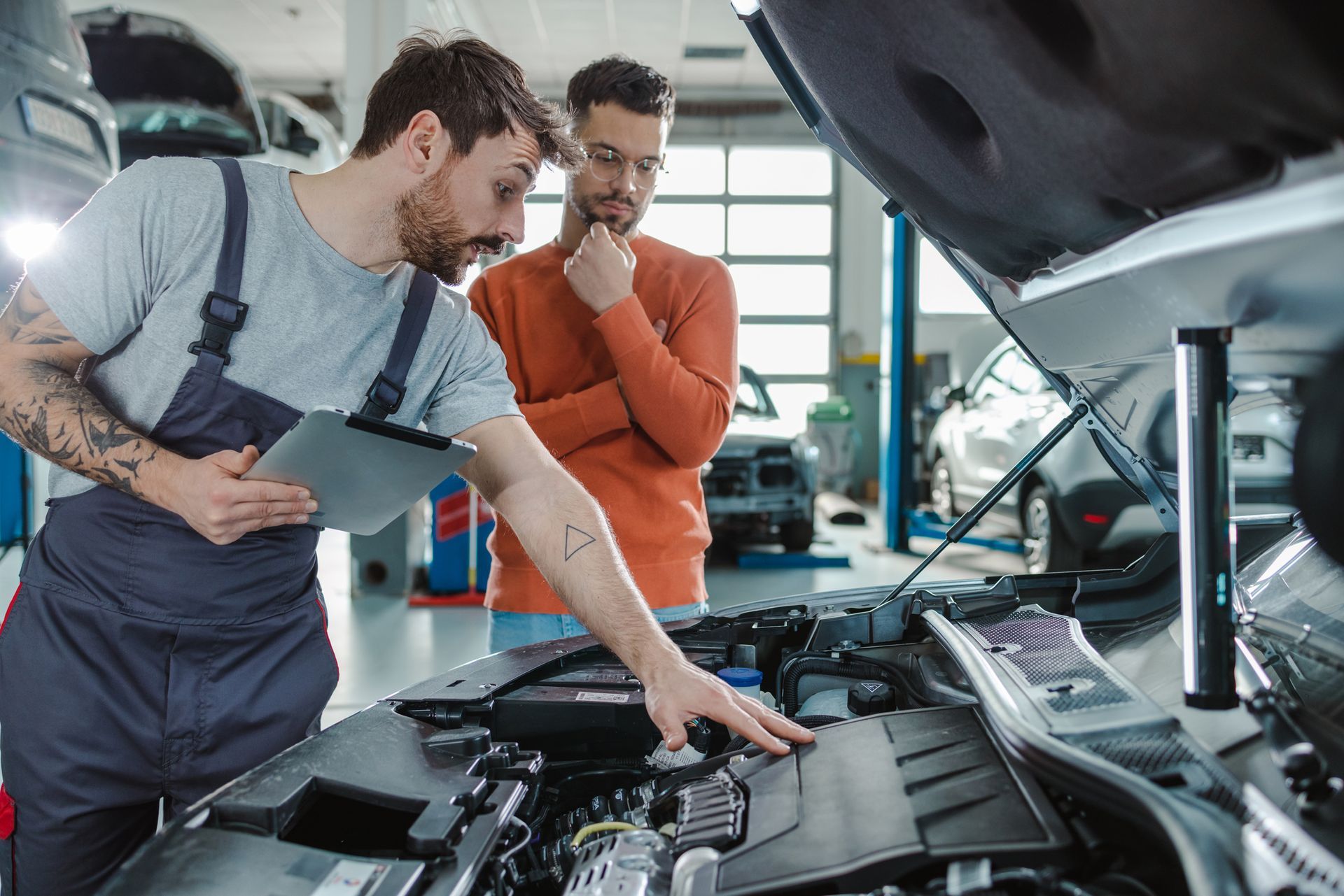 Mechanic showing car engine to a customer in a repair shop.