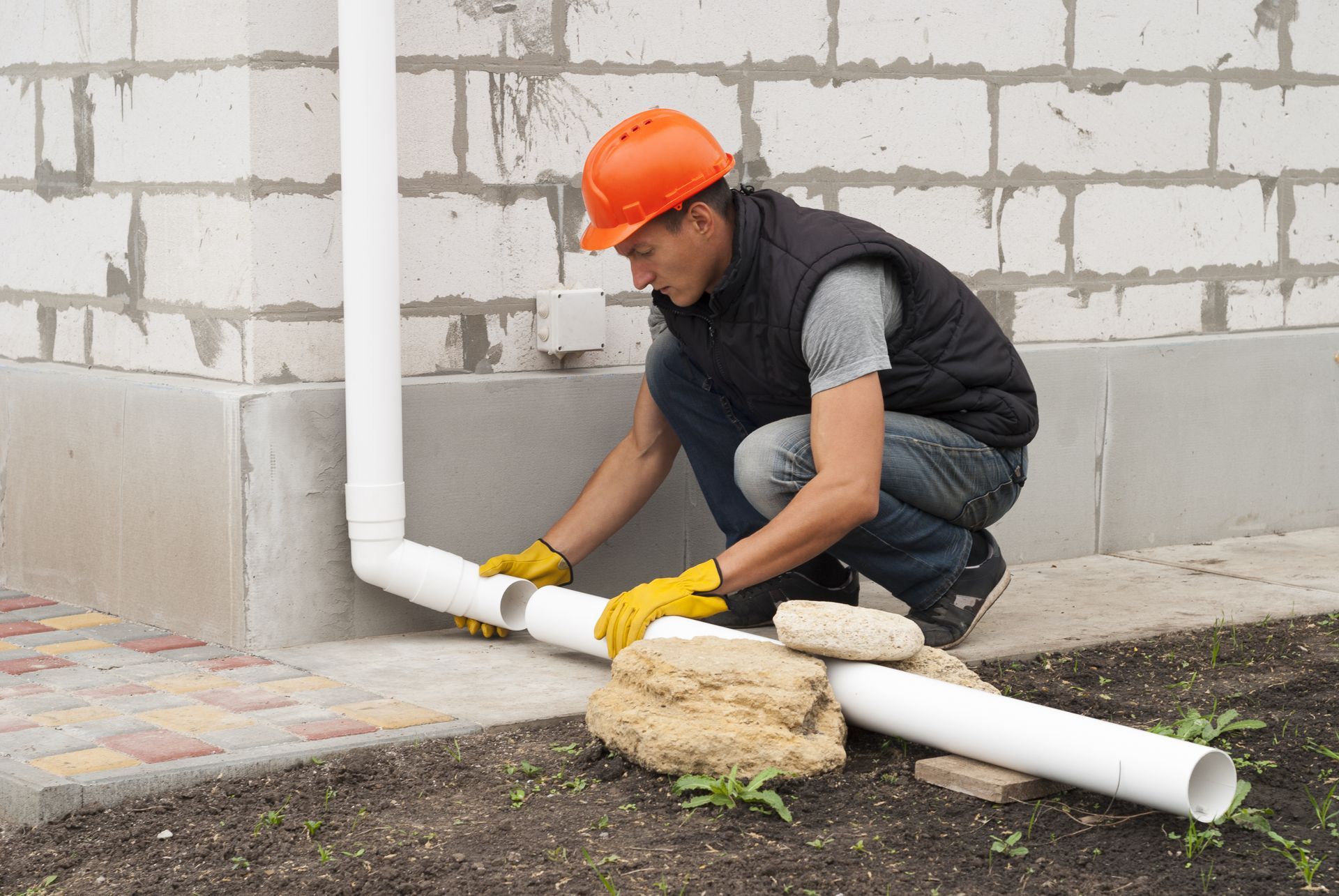 A man is installing a drain pipe on the side of a building.