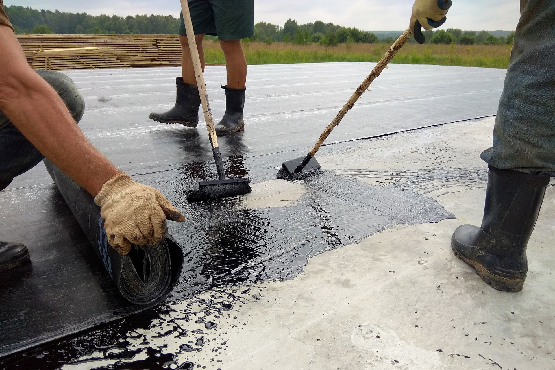 Two men are working on a roof with a roller and a broom.