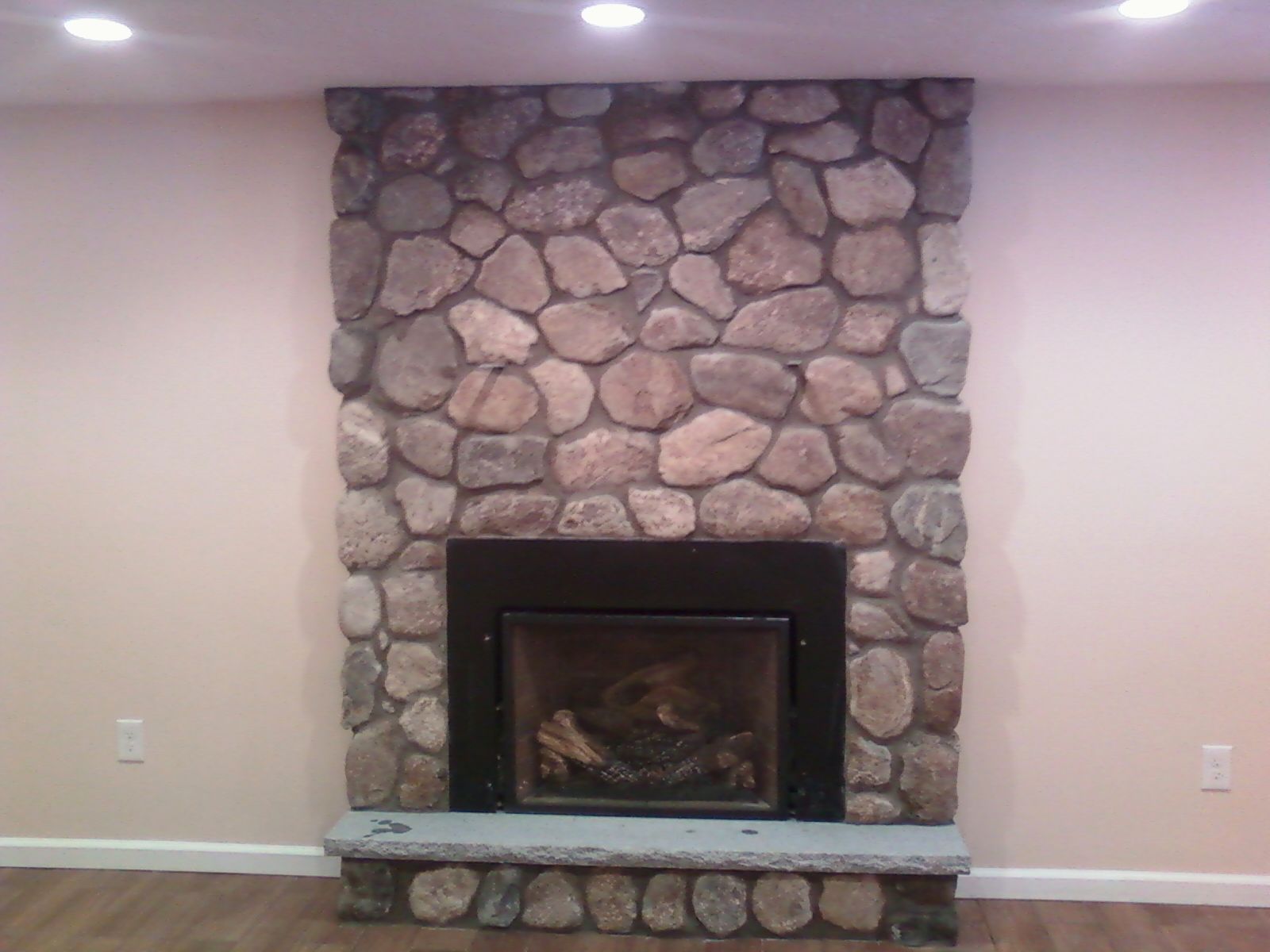 Fireplace with stone facade in a room with beige walls and dark floor.