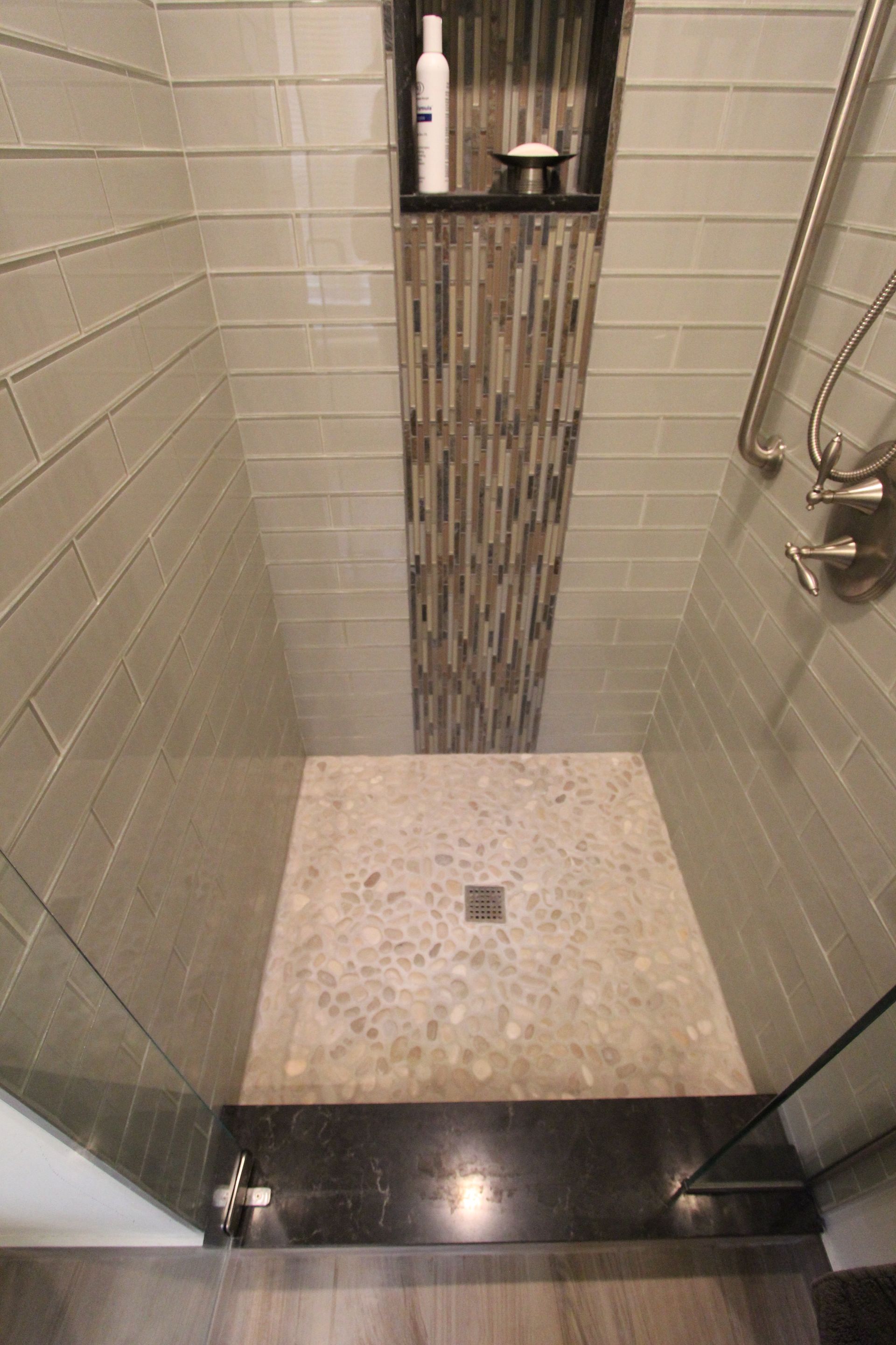 Shower with tiled walls, a stone floor, built-in shelf with toiletries, and a glass door.