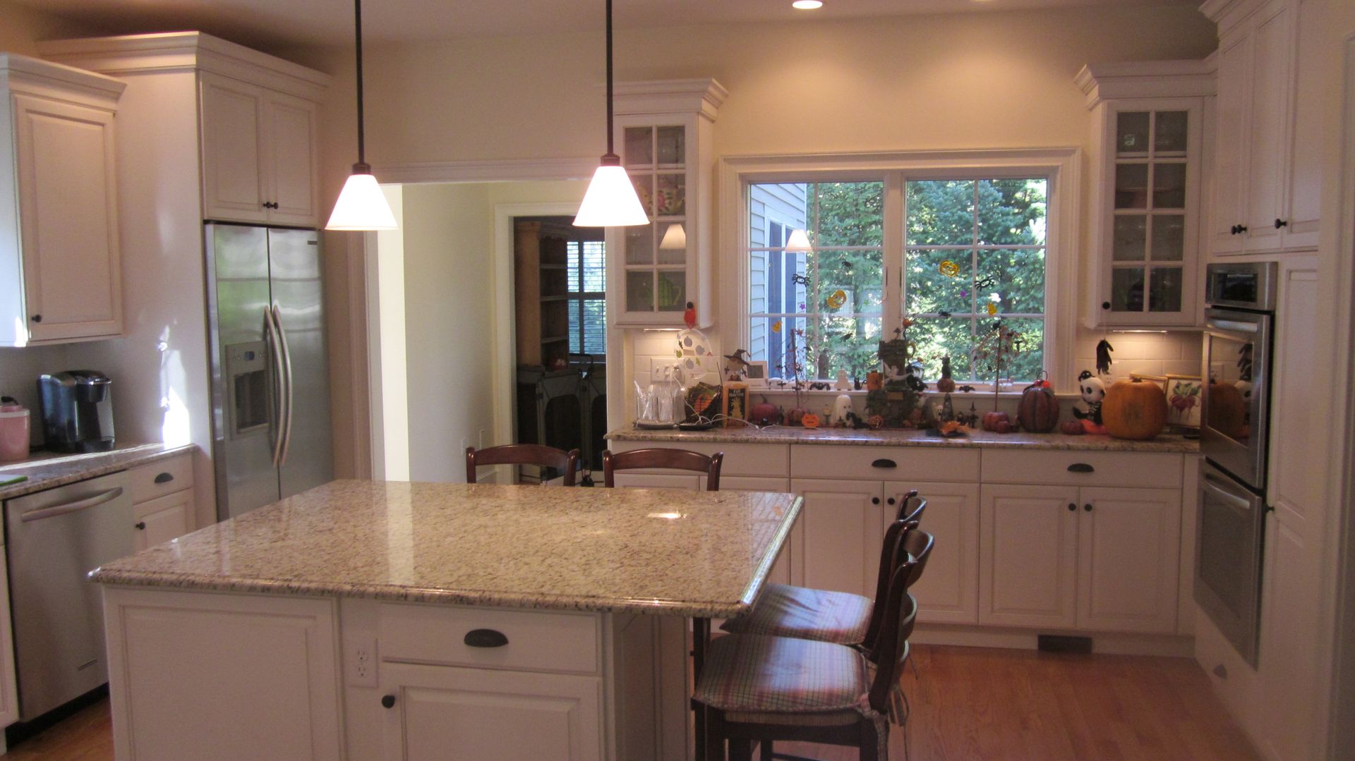 White kitchen with granite island, stainless steel appliances, and window overlooking greenery.
