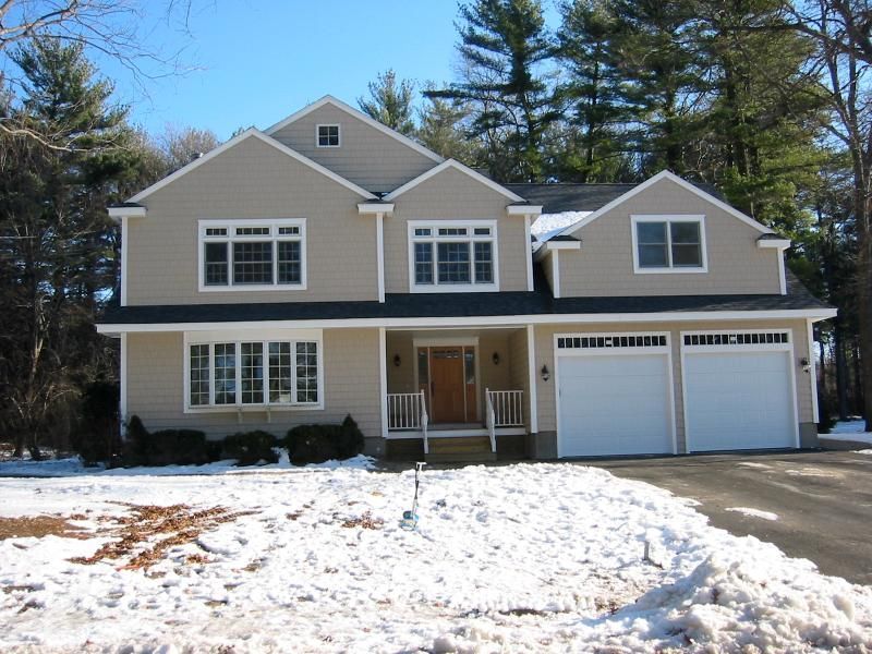 Beige two-story house with white trim, two-car garage, and snow-covered yard.