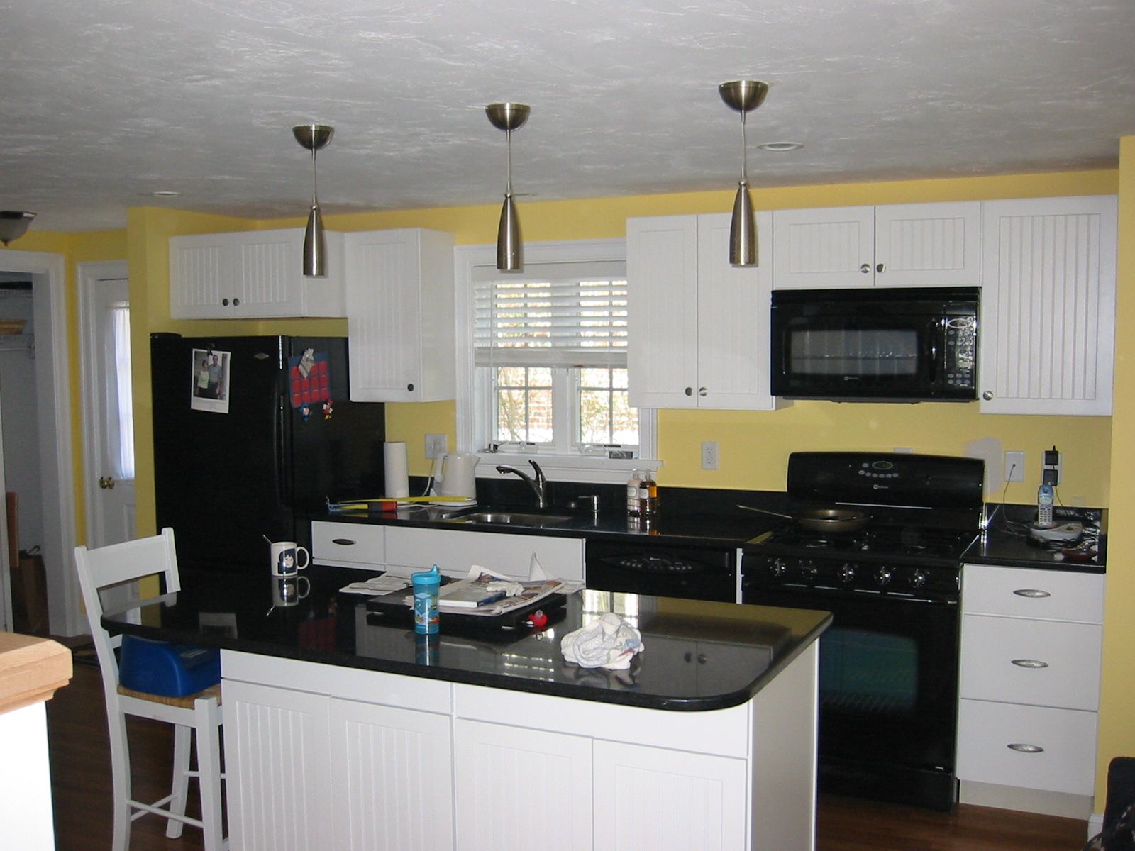 Kitchen with black appliances, white cabinets, yellow walls, and a black countertop island.
