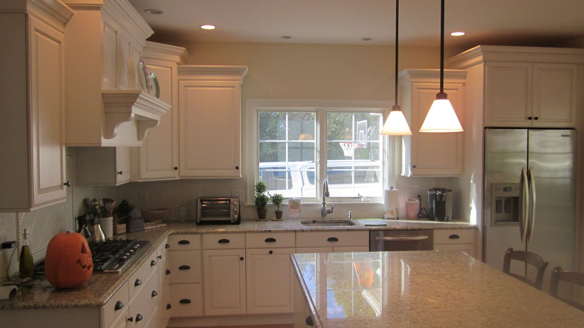 White kitchen with granite countertops, cabinets, and island. A window, appliances, and pumpkin are present.