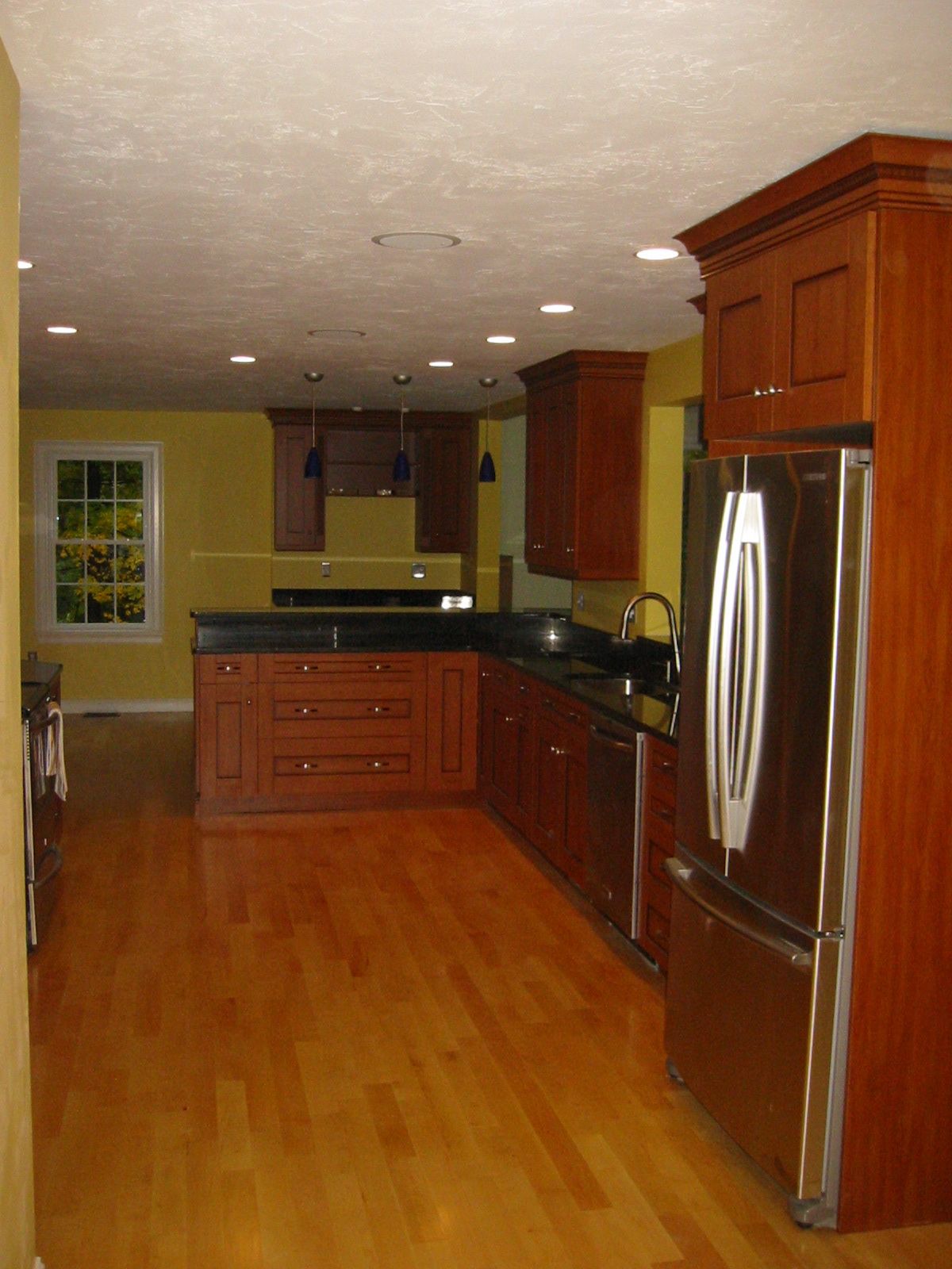 Wooden kitchen with island, cabinets, stainless steel refrigerator, and yellow walls.
