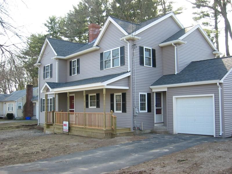 Two-story light gray house with porch, garage, and black shutters. Asphalt driveway leads to the garage.