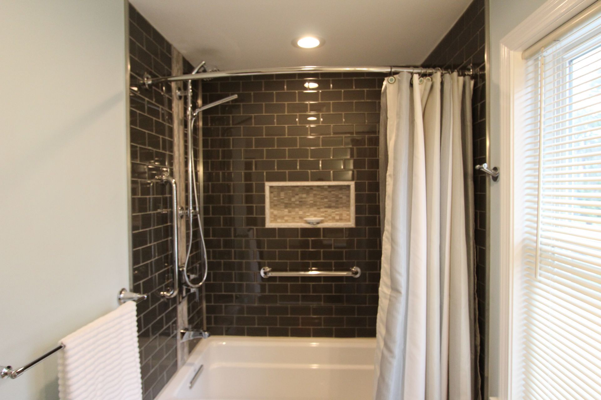Bathroom with dark tiled shower, grab bars, shower curtain, and white tub.