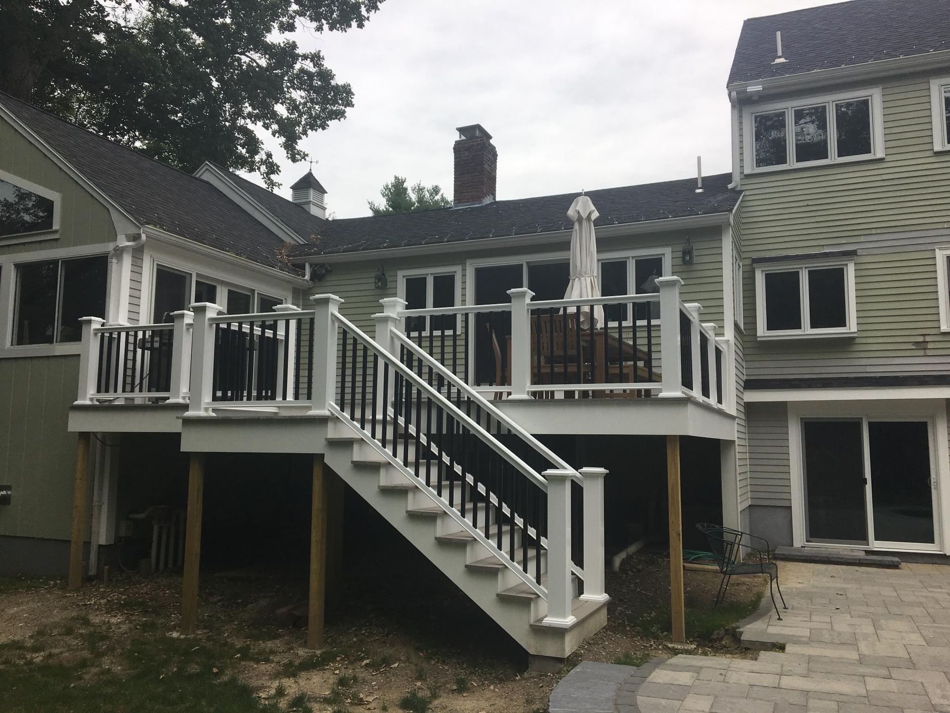 Deck with white rails, black balusters, and stairs leading to a light green house, cloudy sky.