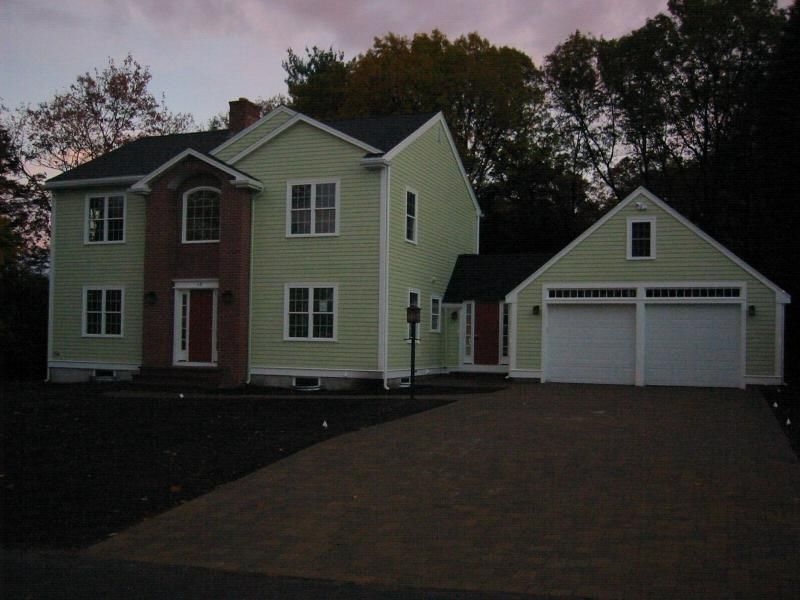 Two-story house and garage with light green siding, red front door, and driveway, at dusk.