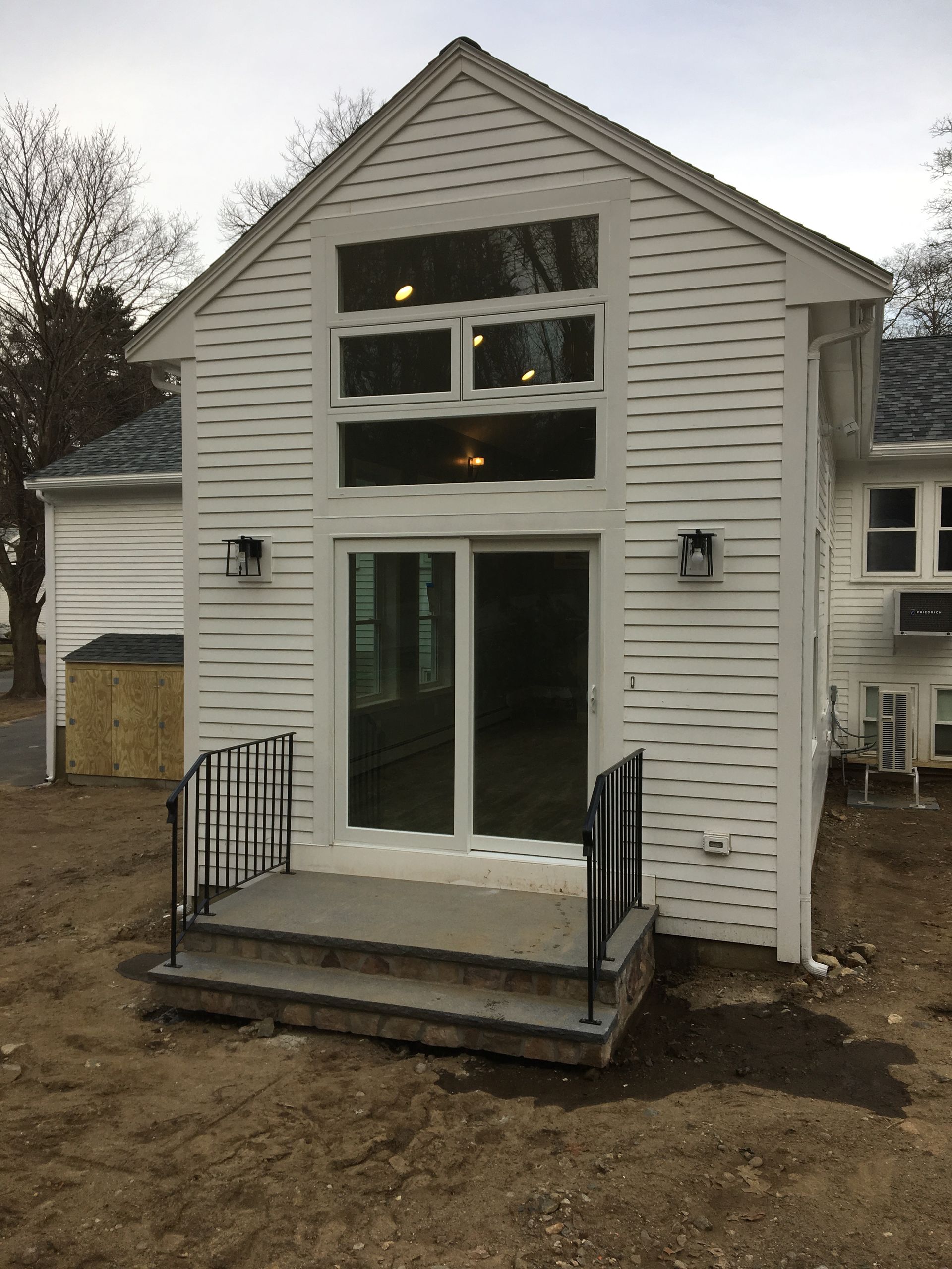 White house addition with large windows, sliding glass door, small porch, and black railing.