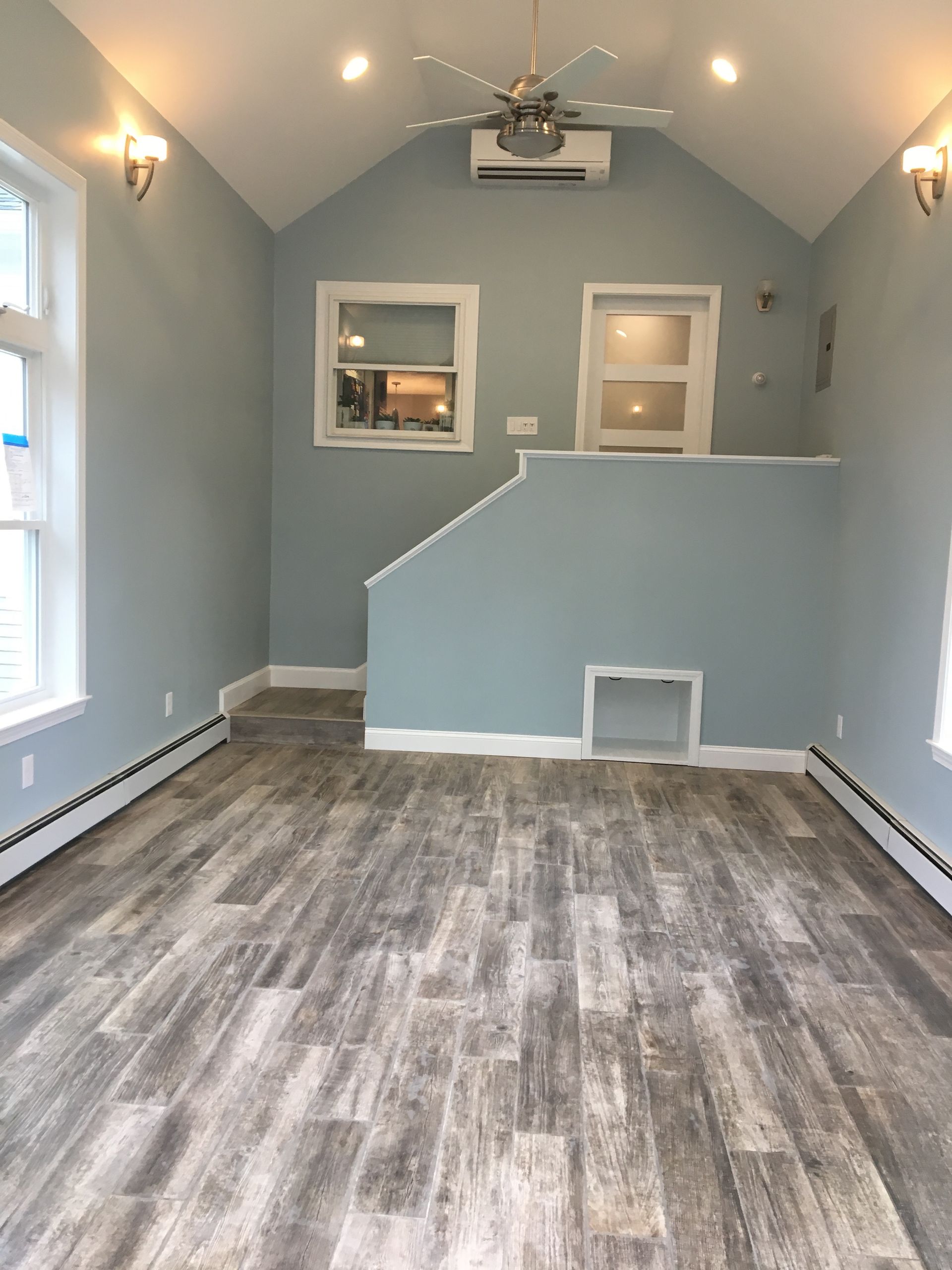 Light blue interior room with wood-look flooring, small windows, and a partial wall leading to an elevated area.