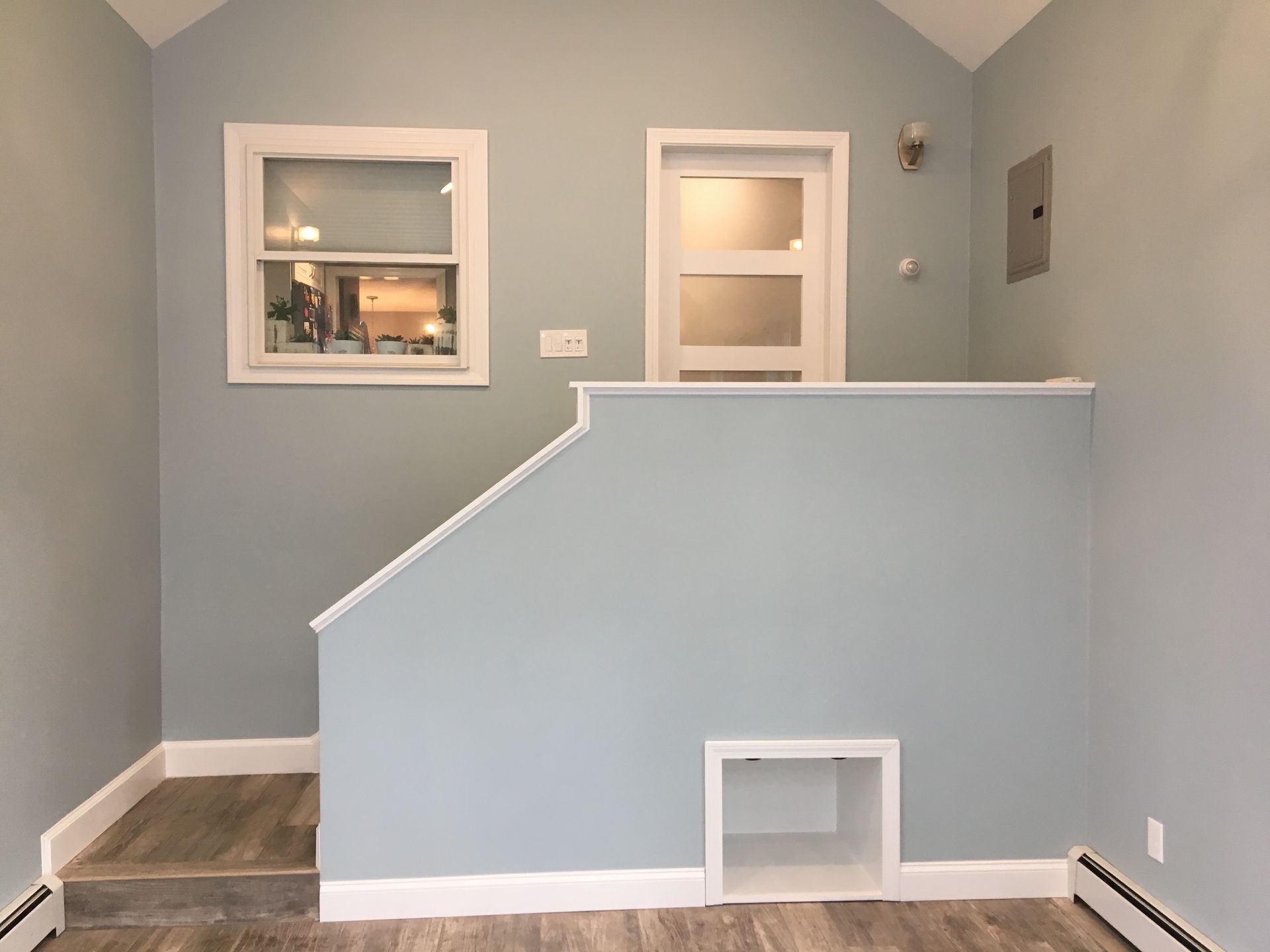 Light blue room with small staircase, window, and door. White trim and a small built-in cubby.