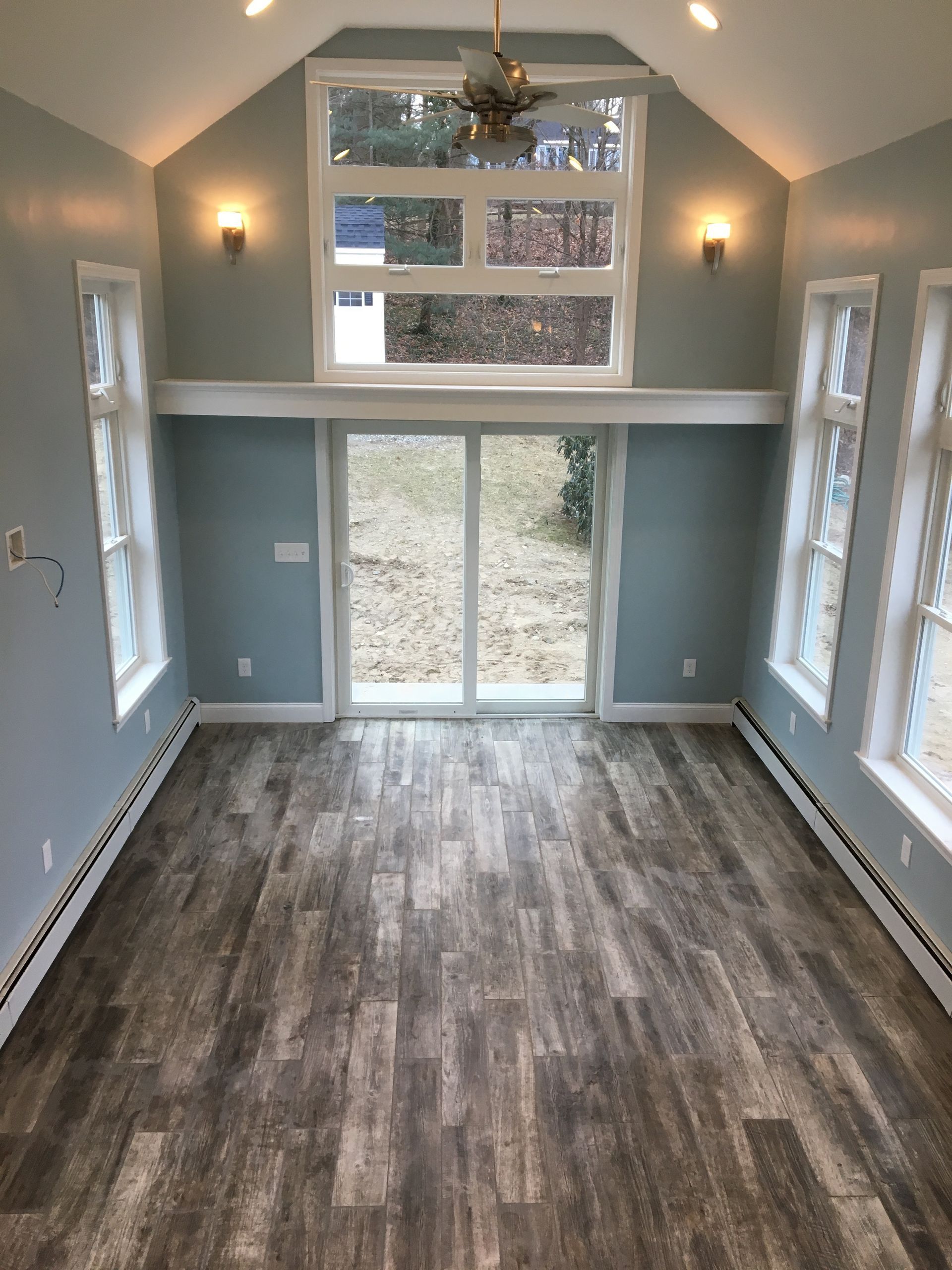Interior of a light blue room with wood-look floors, large windows, and a sliding glass door overlooking a backyard.