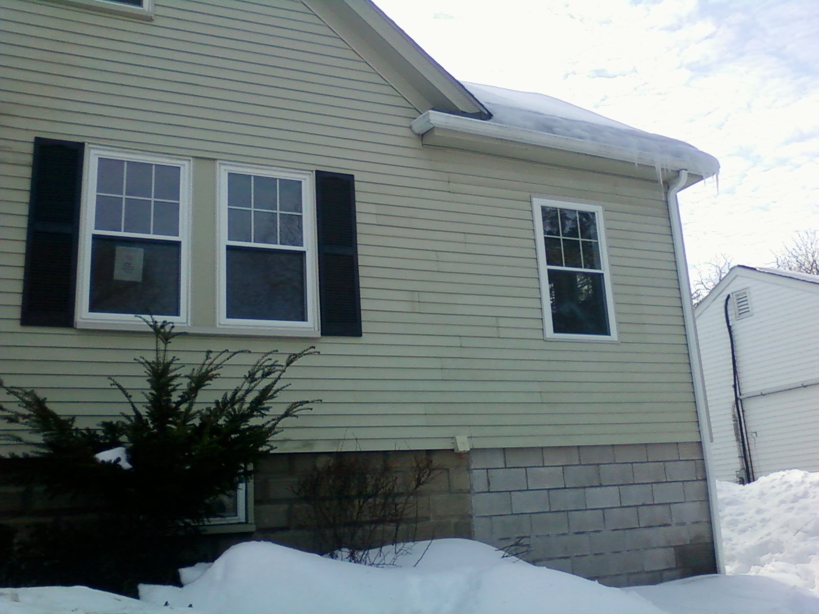 Beige house with snow, black shutters, and icicles.