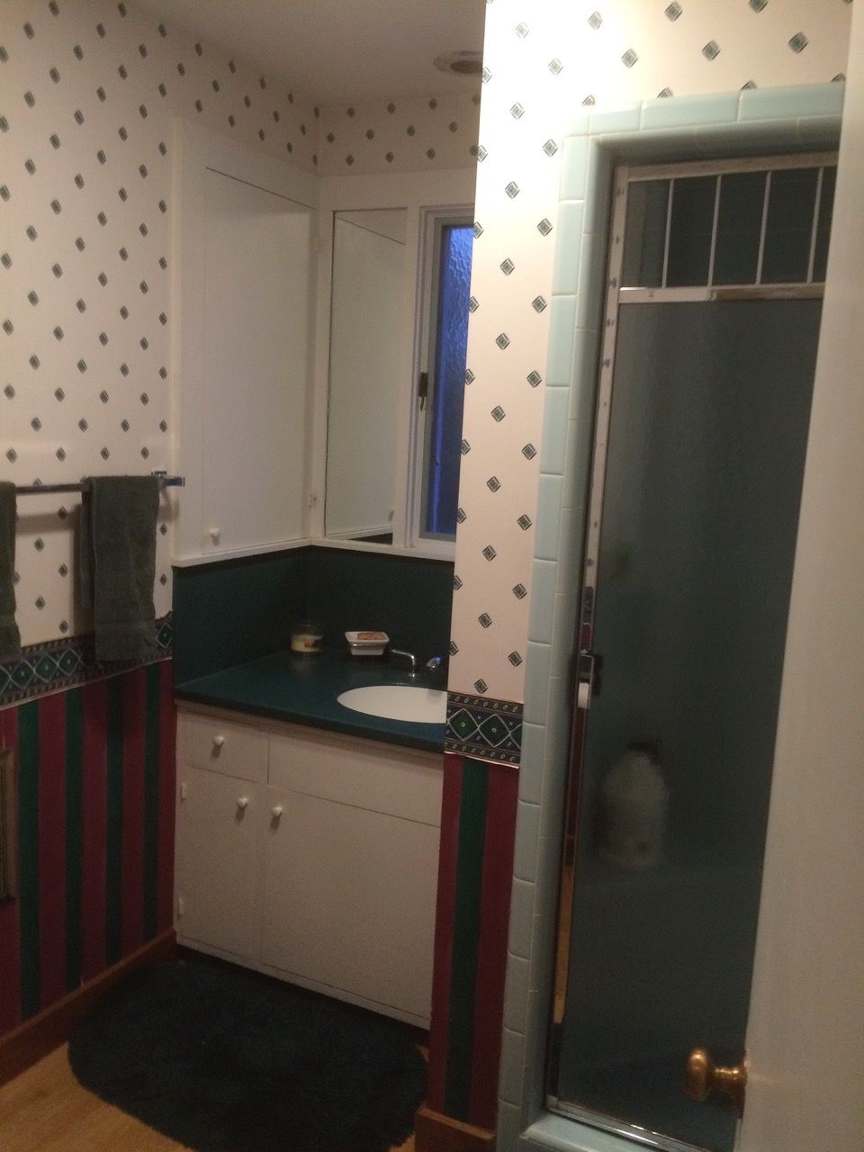 Bathroom with patterned wallpaper, vanity, shower, and a closed door.