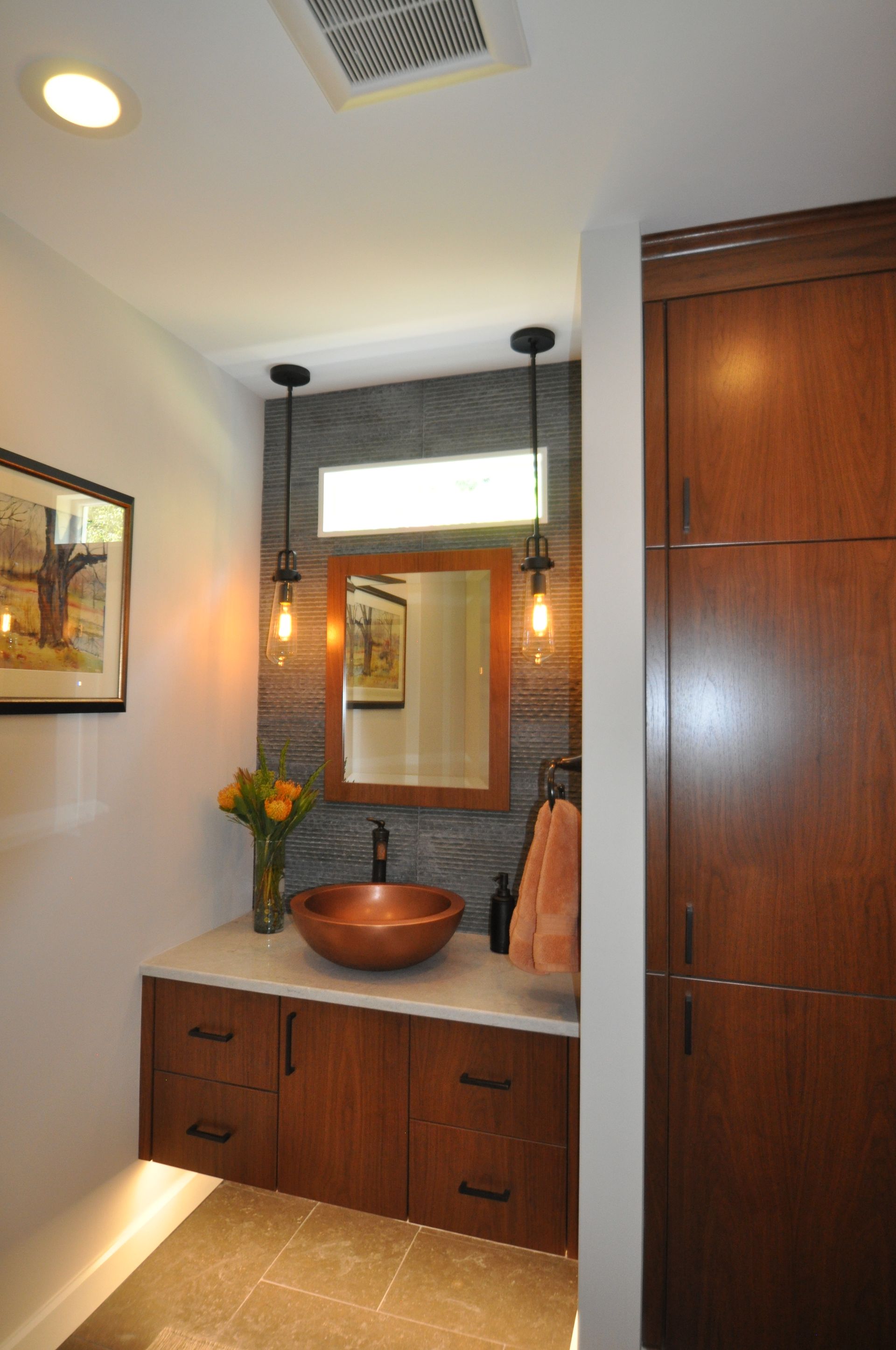 Bathroom with a wooden vanity, copper sink, and modern pendant lights.