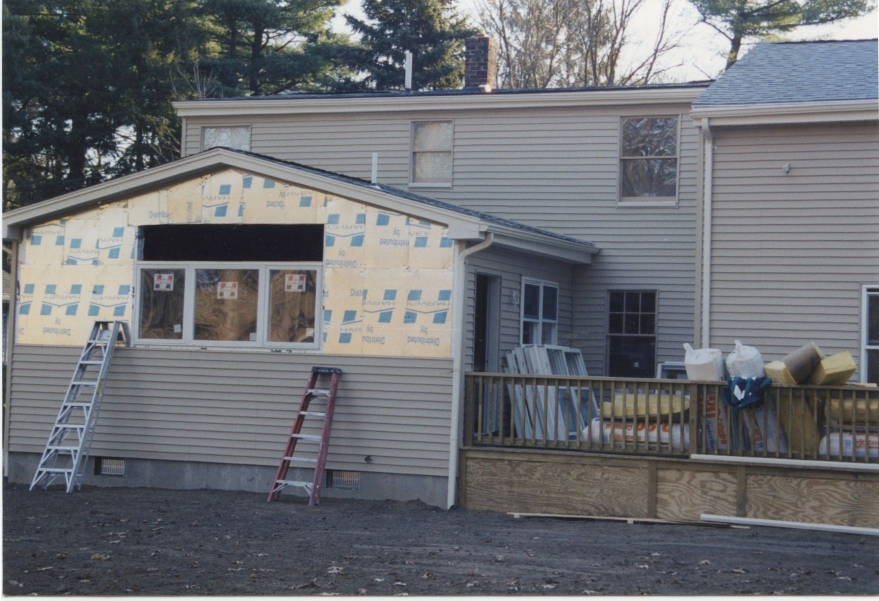 House under construction; addition with windows, siding, and sheathing visible. Ladders lean against the exterior.