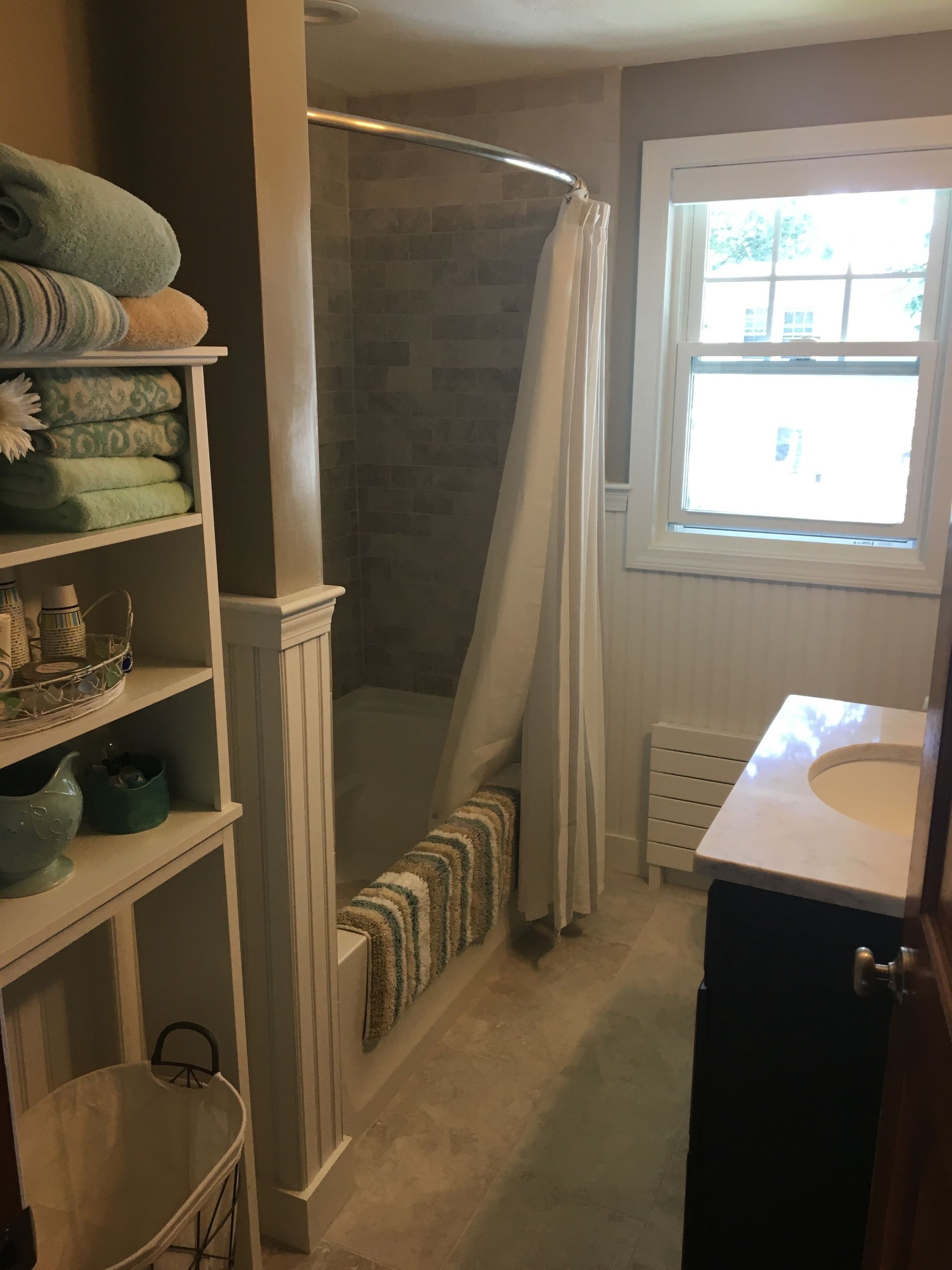 Bathroom with a shower, white vanity, and a shelving unit filled with towels.