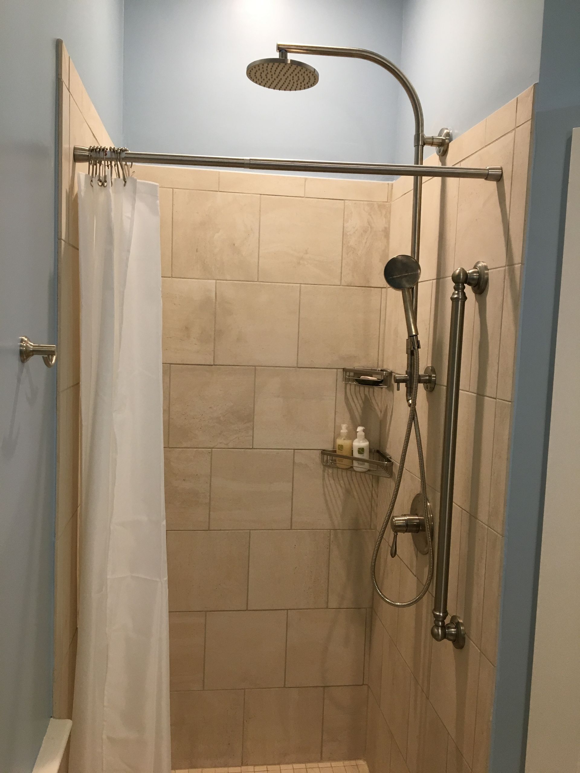 Shower with beige tiled walls, showerhead, and curtain.