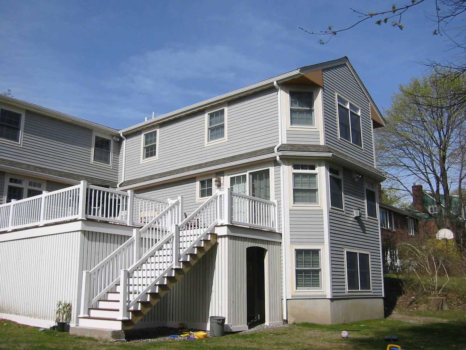 Two-story house with gray siding and white deck with stairs leading to a backyard with grass.