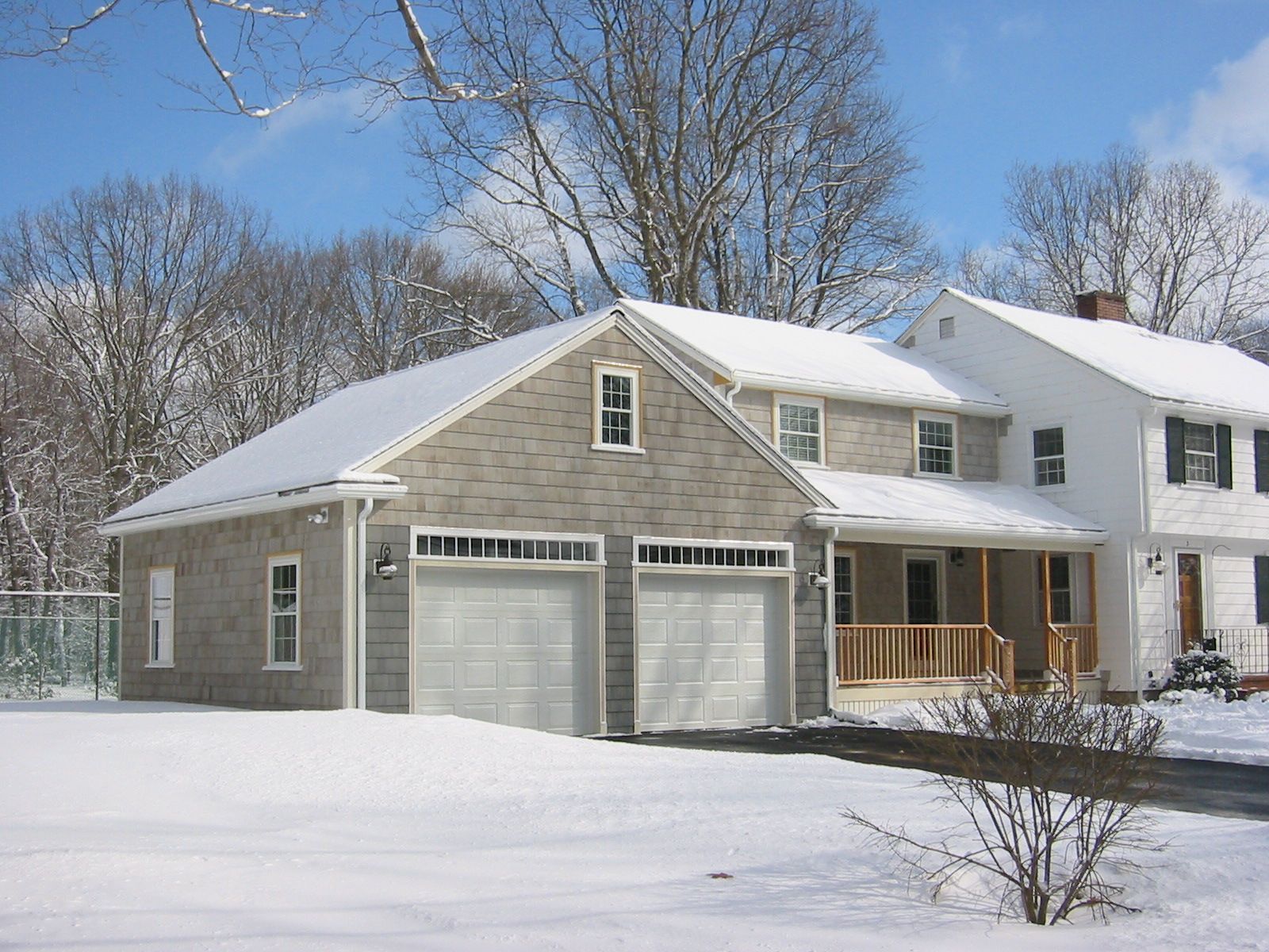 Snow-covered house with a two-car garage. Winter scene with bare trees and a cloudy sky.